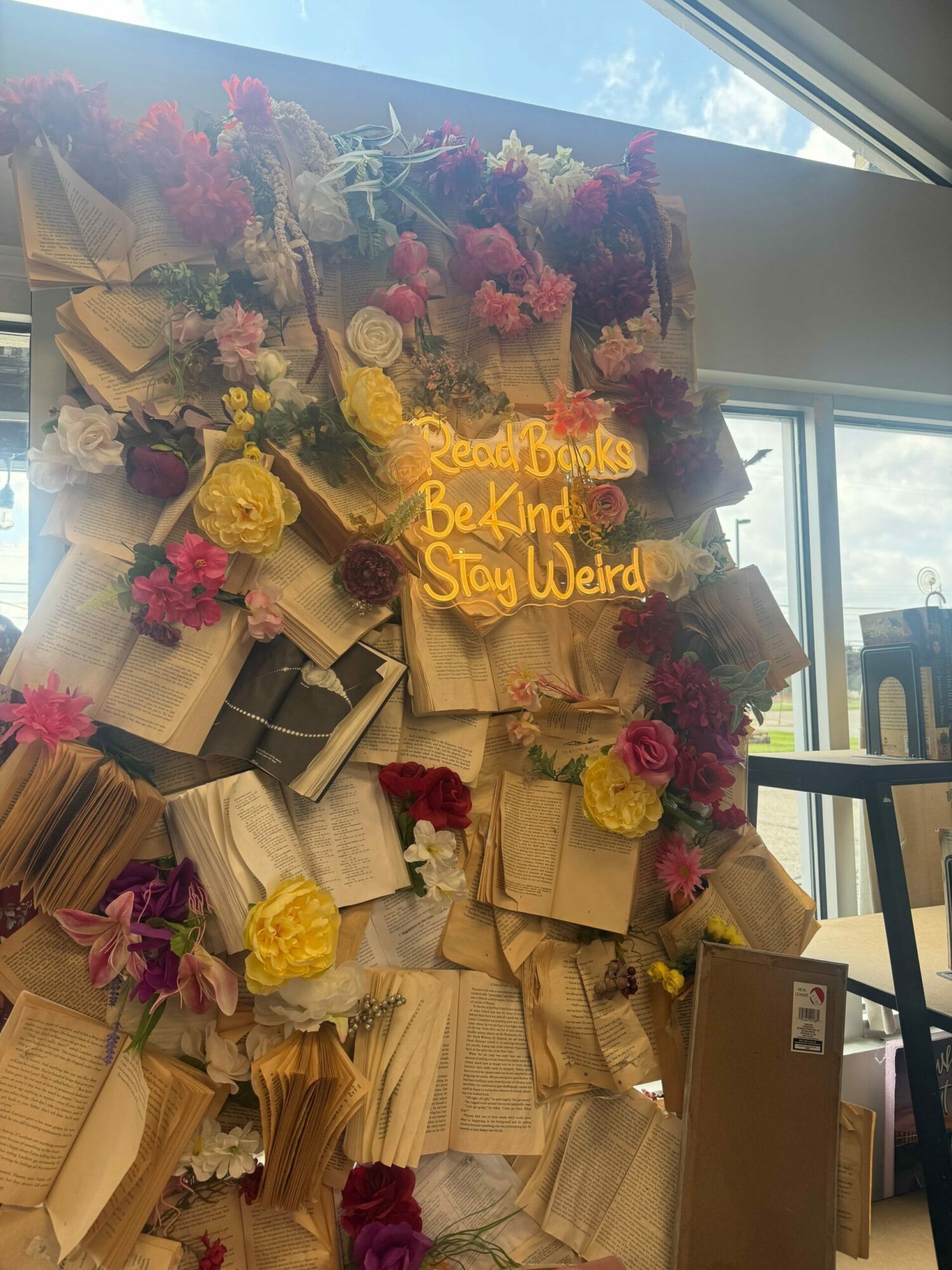 Table with floral arrangements, paper bags, and a sign reading 'Rest in Power Breonna Taylor,' in front of windows.