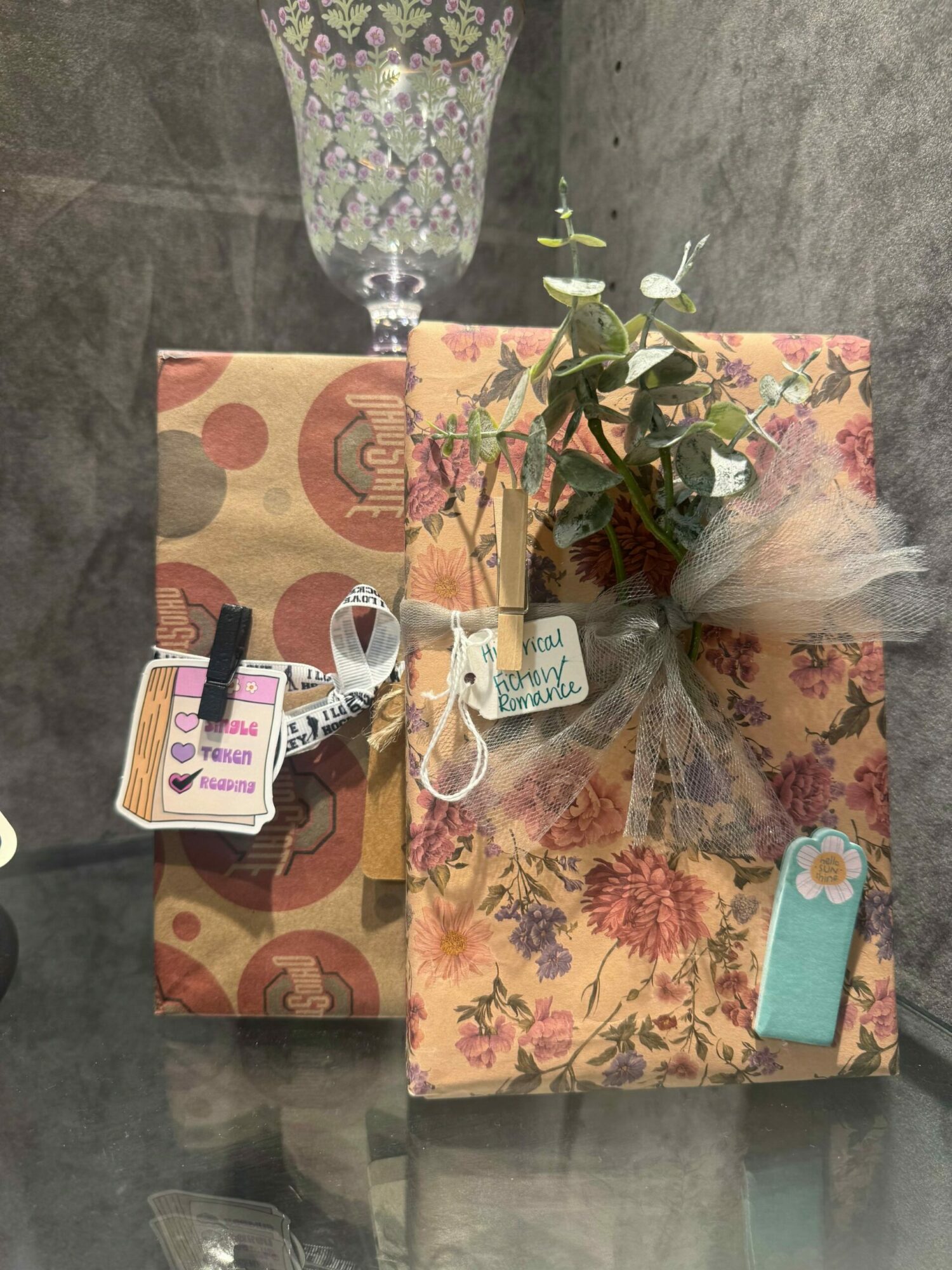 Two wrapped gift boxes with tags and a flower on top, placed on a concrete surface.