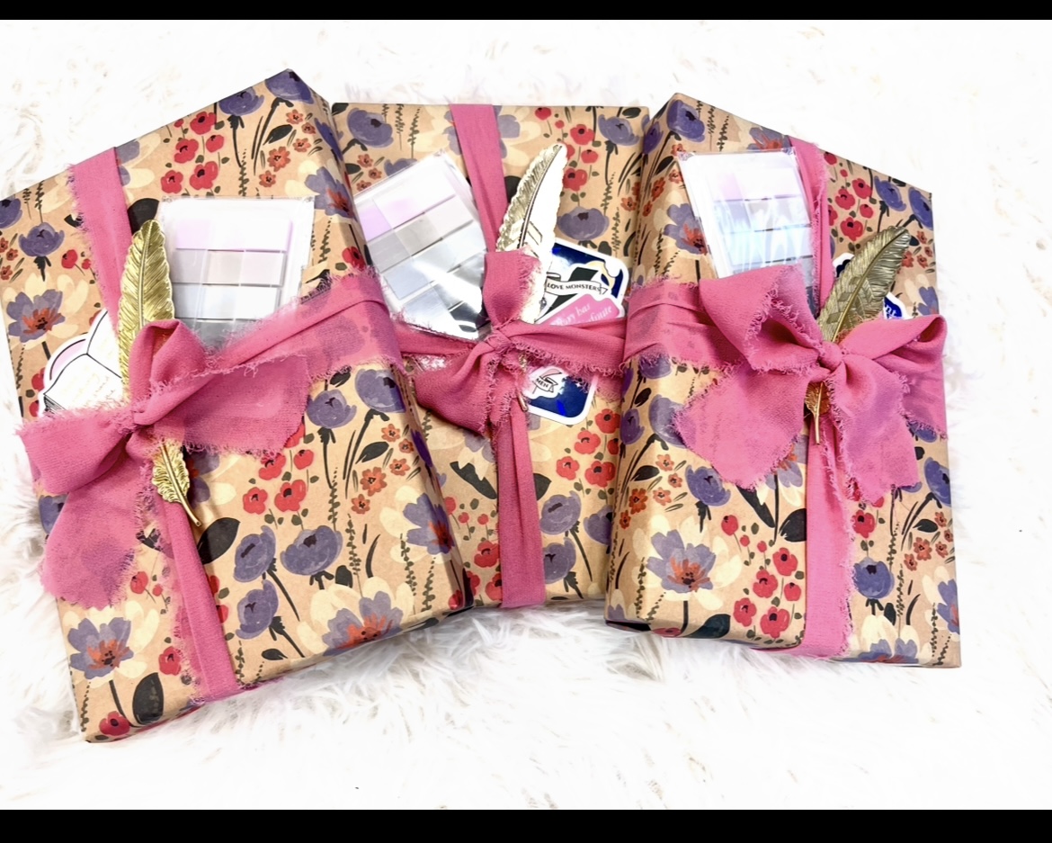 Three decorative gift boxes wrapped in floral paper with pink ribbons and bows, arranged side by side.