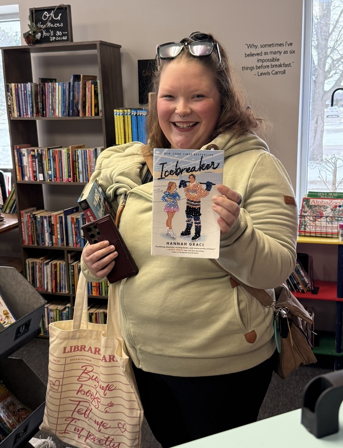 Smiling girl holding a book titled 'Icebreaker' in a bookstore, with bookshelves and a tote bag nearby.