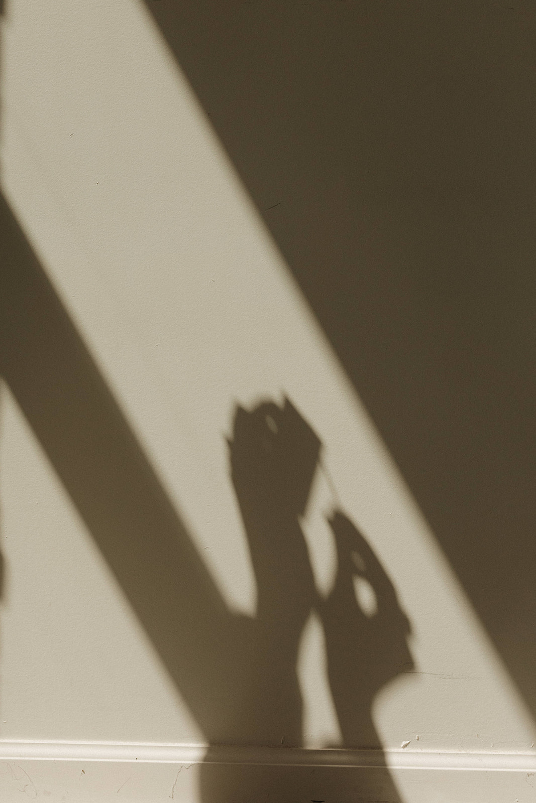 Shadow of a person holding a phone, cast on a wall with light and dark areas, creating a silhouette.