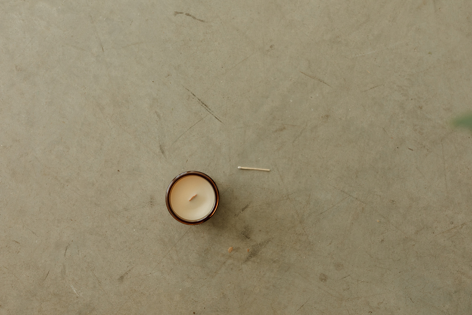 A small candle in a container on a plain surface, with a matchstick nearby.