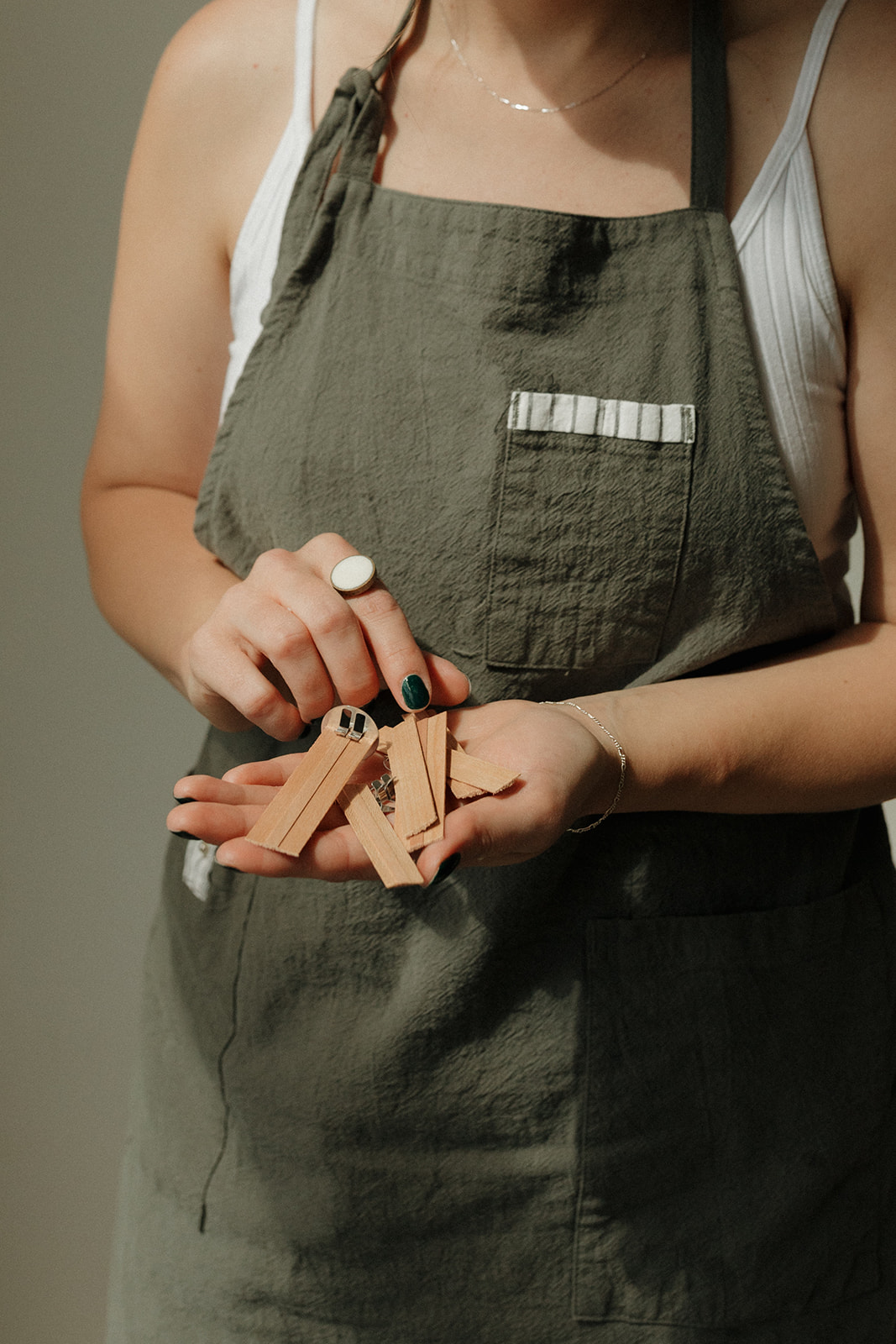 Person wearing a green apron holding clothespins, with a white tank top visible, and a ring on finger.