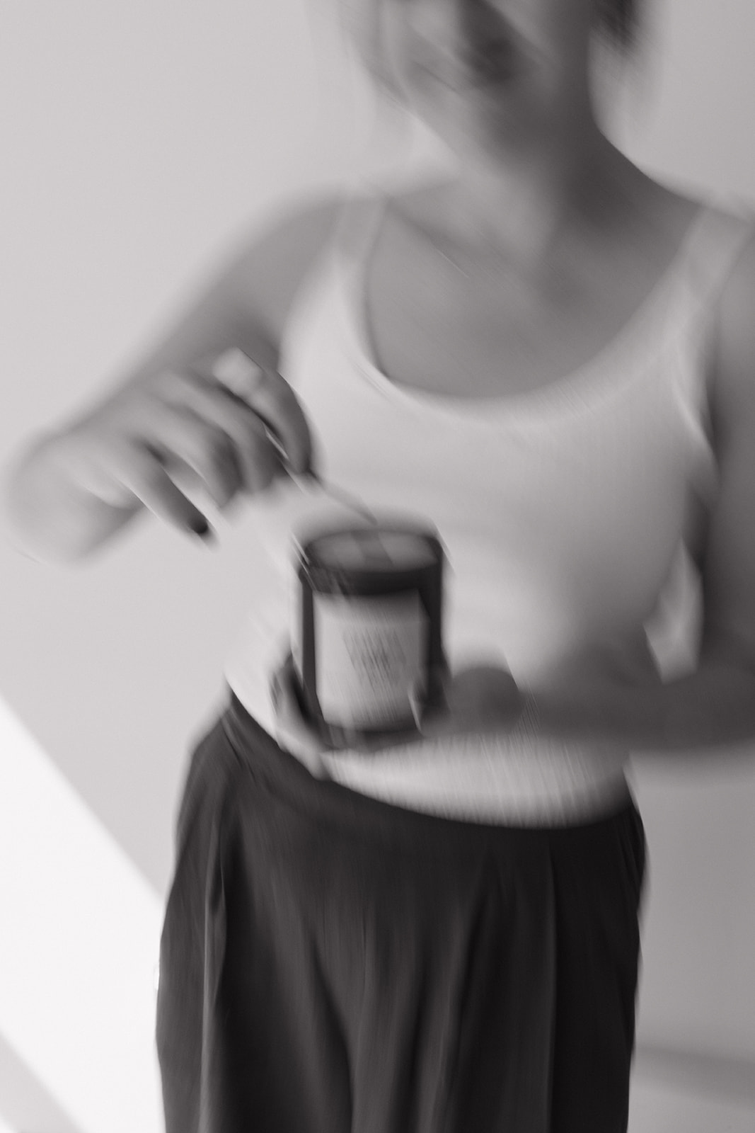 Person in a tank top holding a container, with blurred face and upper body, in black and white.