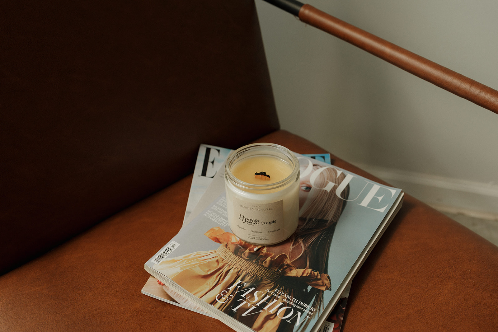 A candle on a magazine resting on a brown leather surface, with a wooden stick above. Alt text word count: 24. Confidence: 0.9