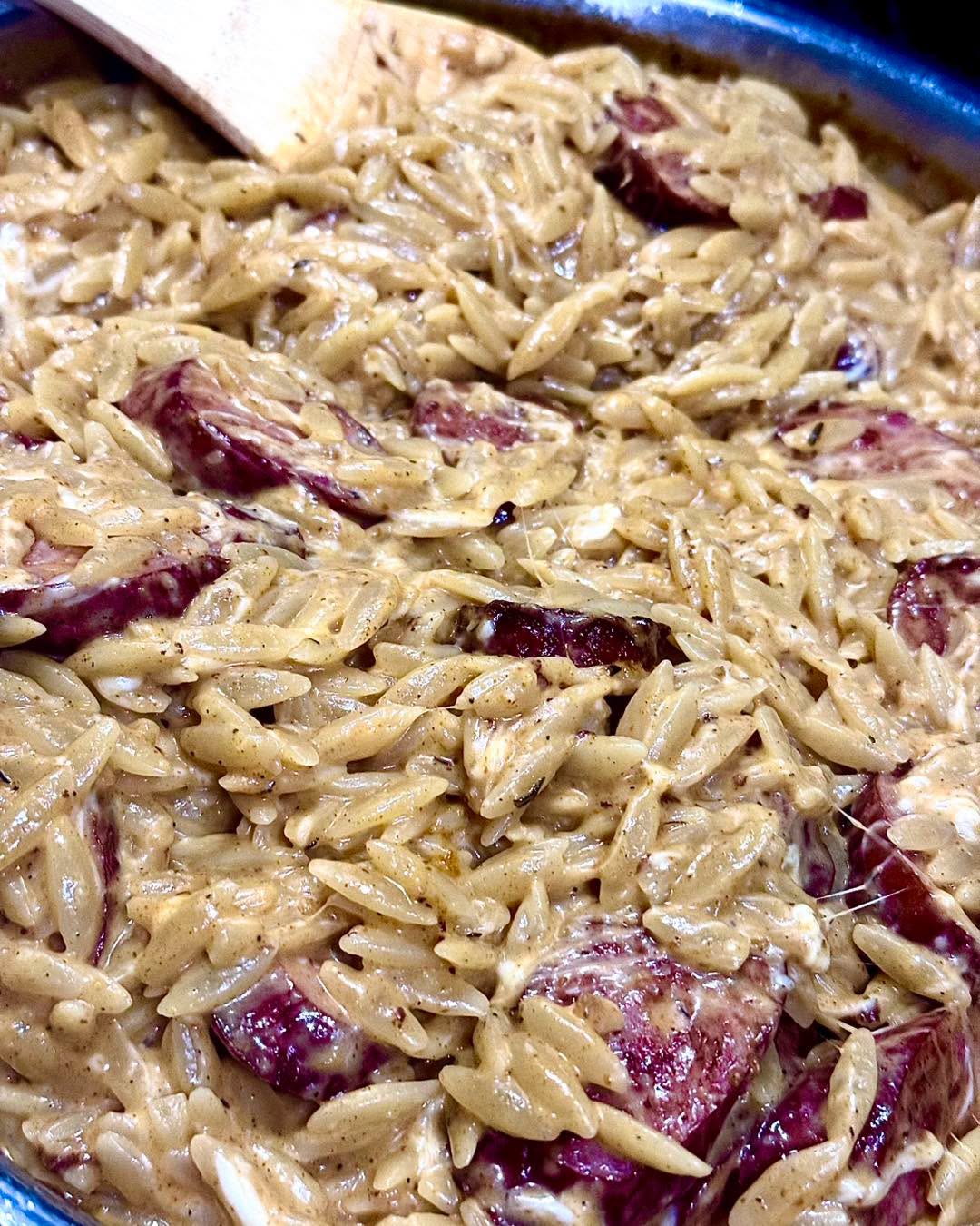 Creamy pasta with pieces of red onion in a pan, with a spatula visible at the top left corner.
