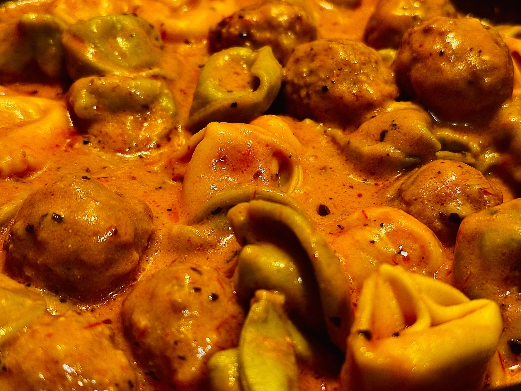 Close-up of cooked meatballs and tortellini pasta in sauce, with green olives visible, in a dish.