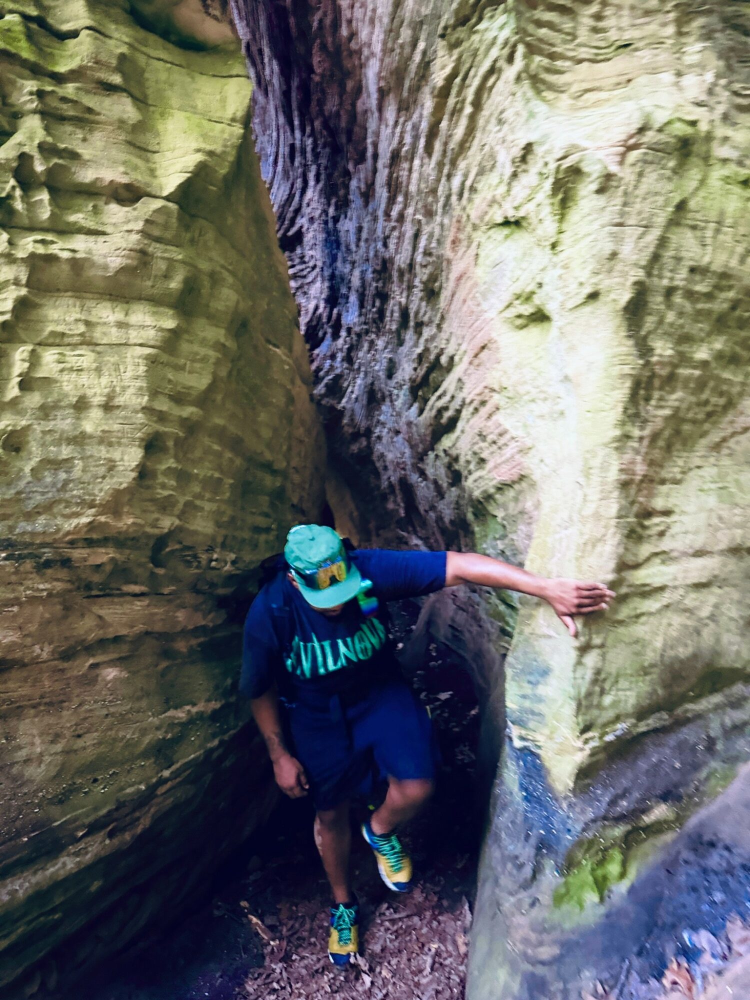 Child wearing a blue hat and clothing, reaching out to touch a rock wall in a narrow canyon.