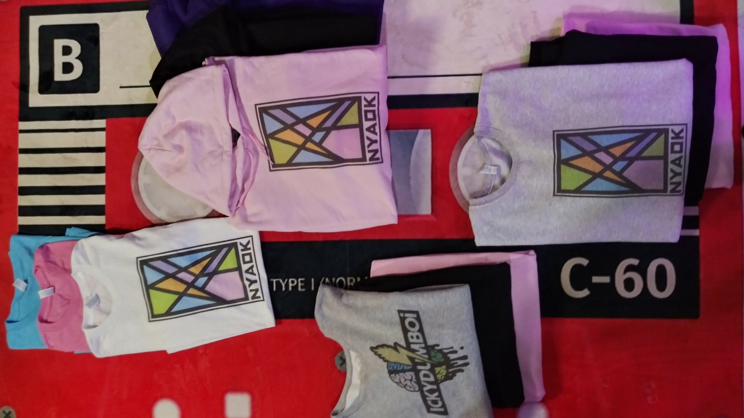 Multiple folded clothing items with colorful tags and labels on a red and black background.