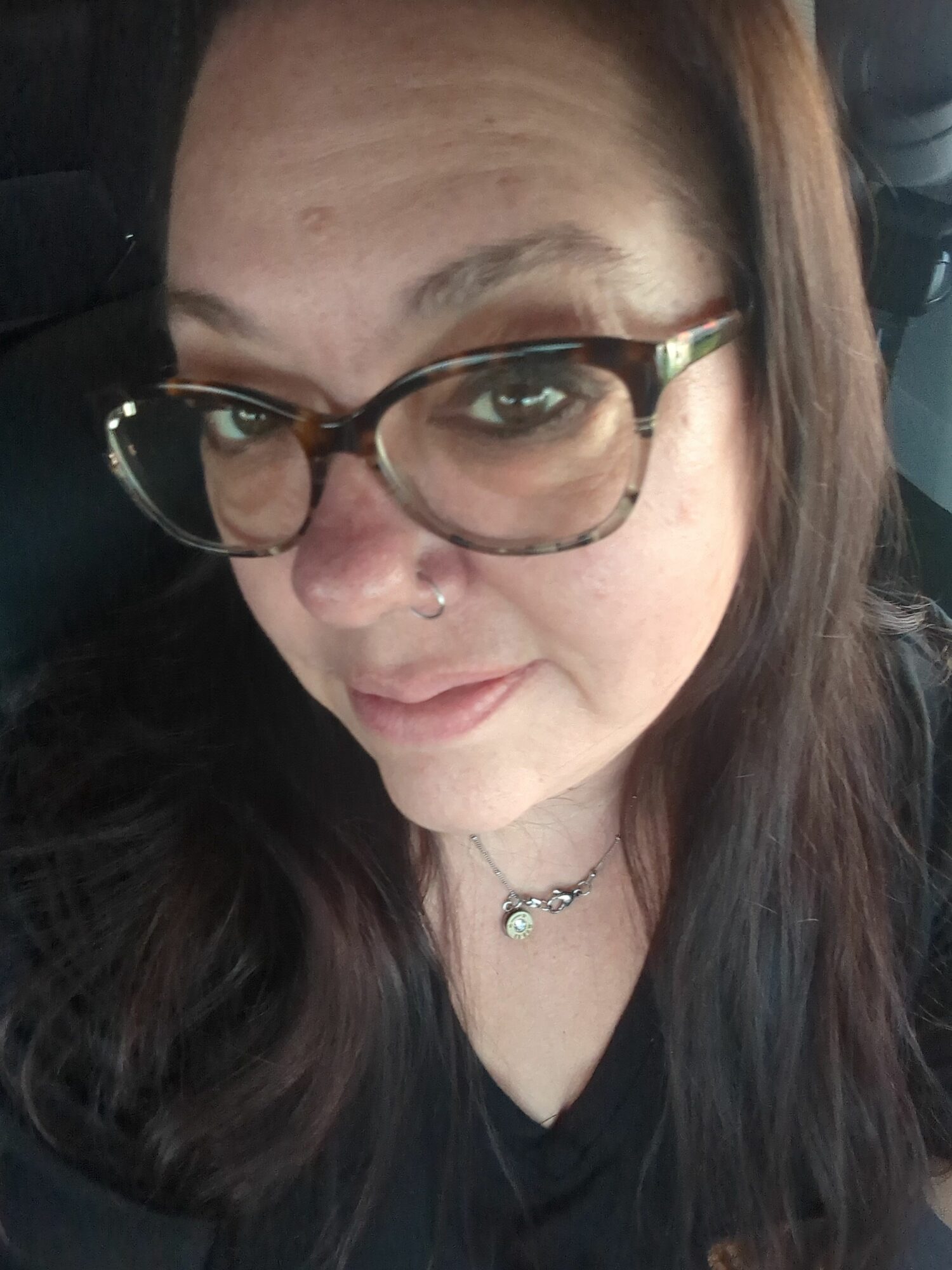 Person with glasses and a nose piercing, lying down with dark hair and a choker necklace.