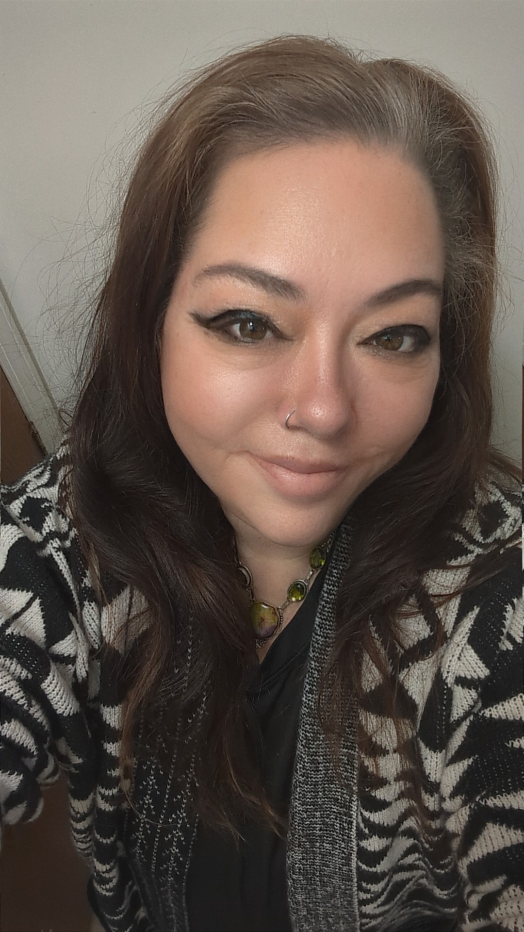 Close-up of a woman with long dark hair, makeup, and a patterned sweater, smiling slightly.