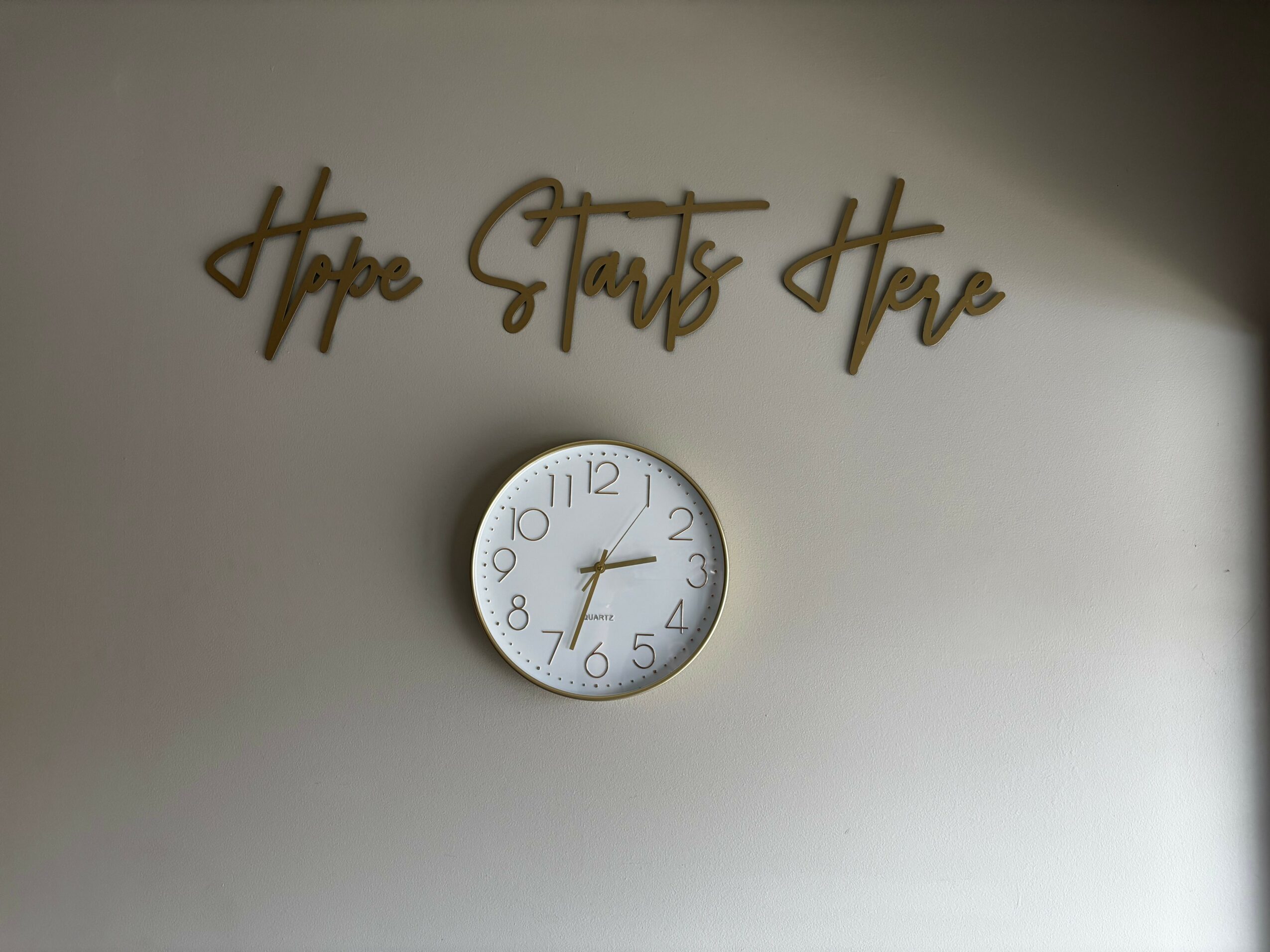Wall with gold cursive sign reading 'Hope Starts Here' and a round clock showing 8:24.