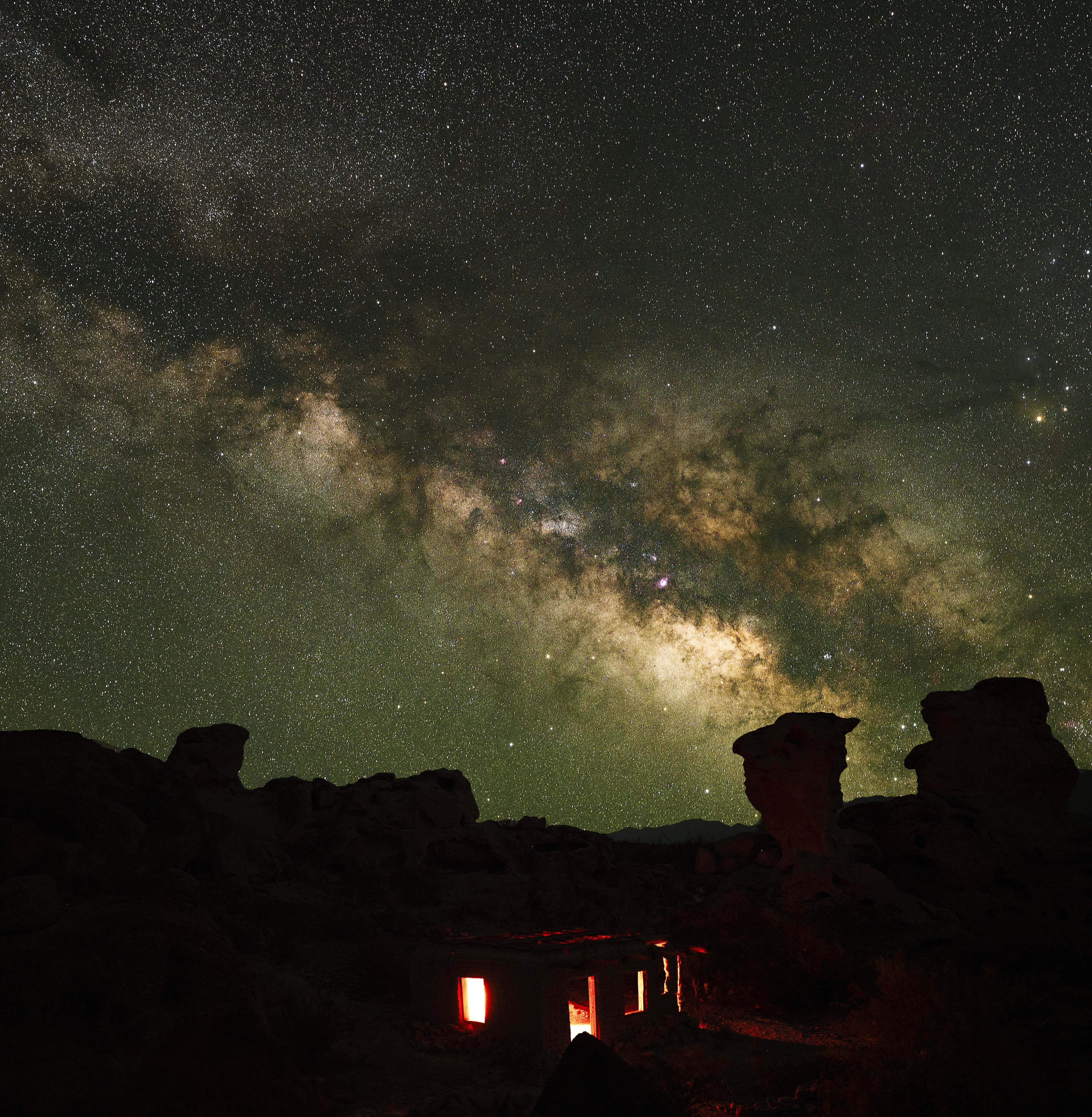 Night sky with stars and the Milky Way galaxy above a rocky landscape with illuminated structures.