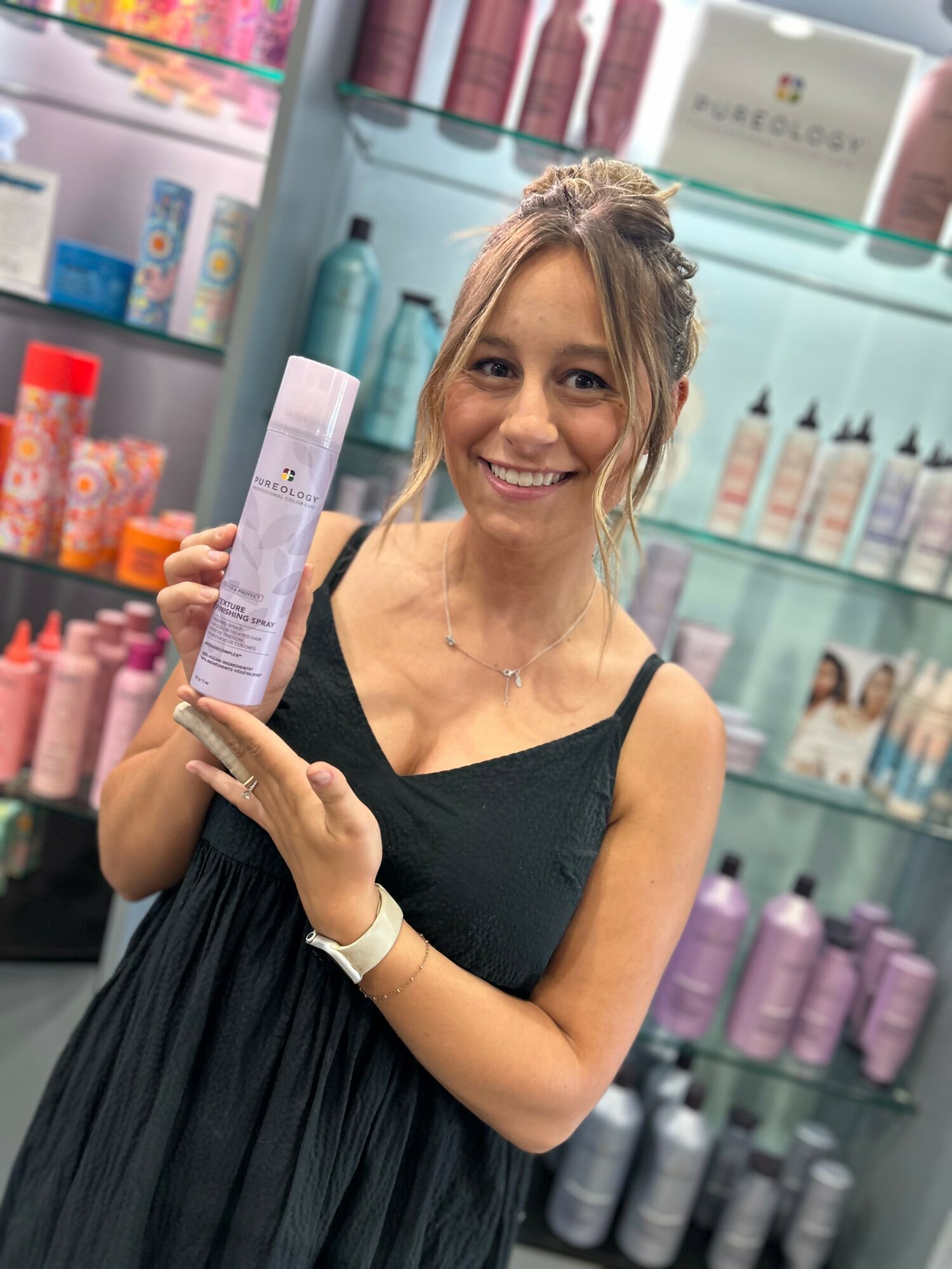 Smiling woman holding a skincare product in a store with shelves of beauty products behind her.