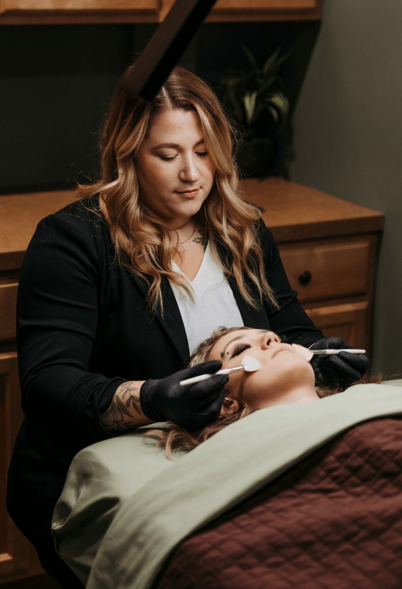 Woman performing a cosmetic procedure on a person lying in a treatment bed, in a clinic setting.