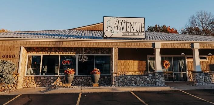 Single-story building with a sign reading 'Avenue' and a parking lot in front, under a clear blue sky.