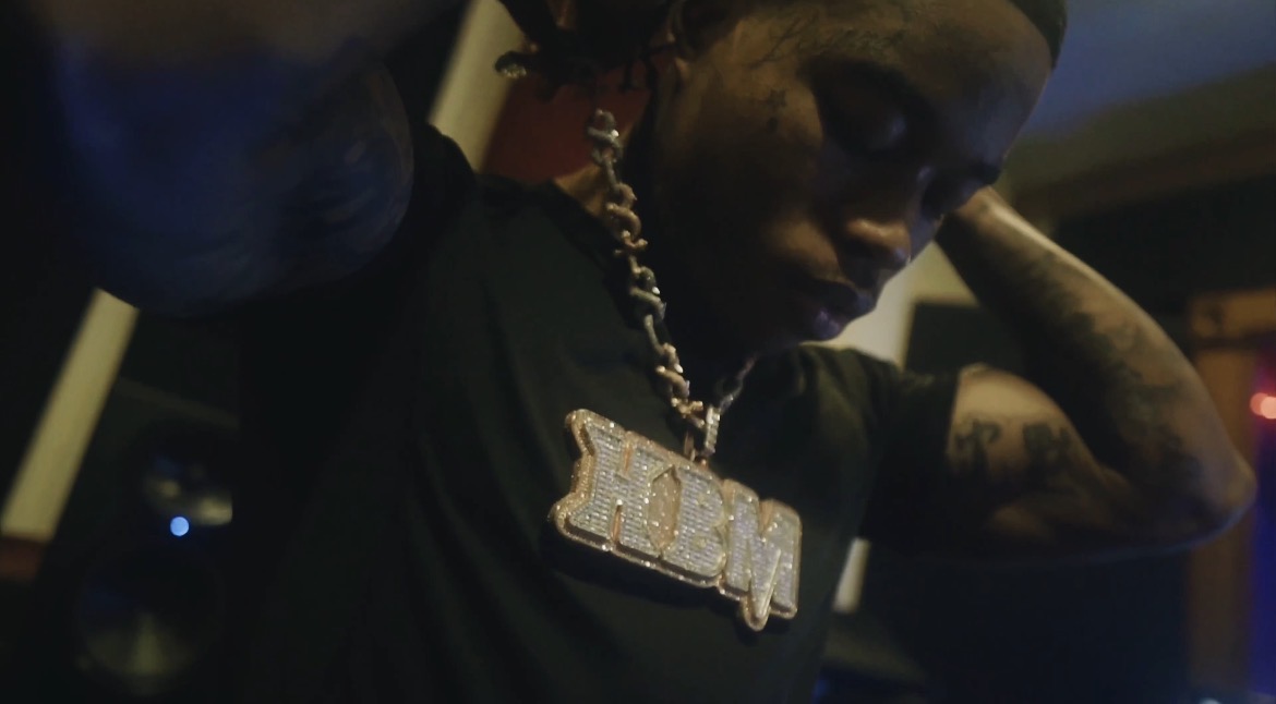 Person with a large chain necklace, adjusting their hair, in a dimly lit environment.