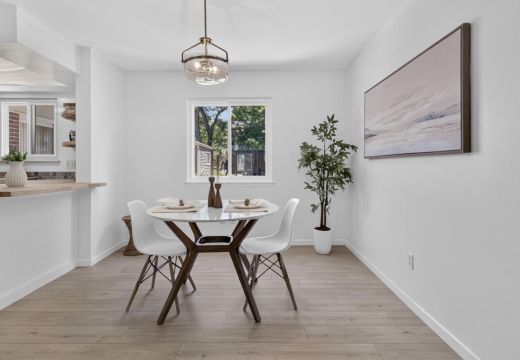 Dining area with a round table, four chairs, a window, a potted plant, and a large wall art piece.