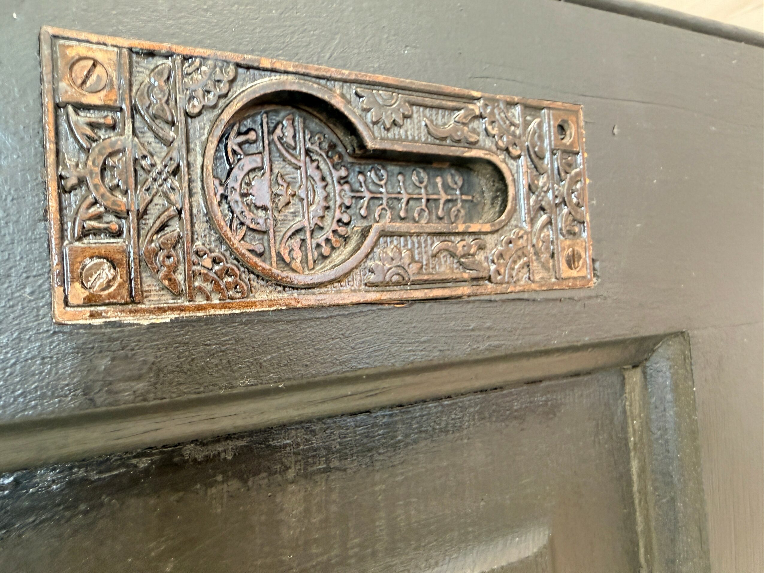 Decorative keyhole plate with intricate patterns and designs, mounted on a gray door surface.