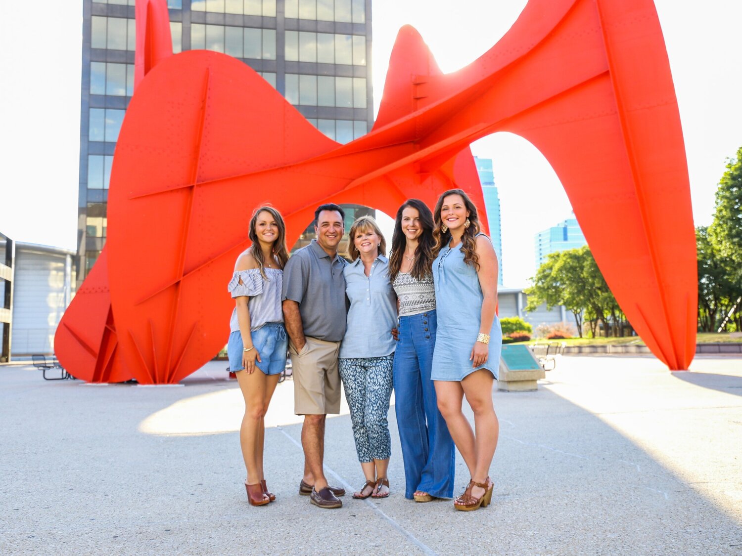 Group of five people standing in front of a large red dragon sculpture outdoors, with buildings in the background.