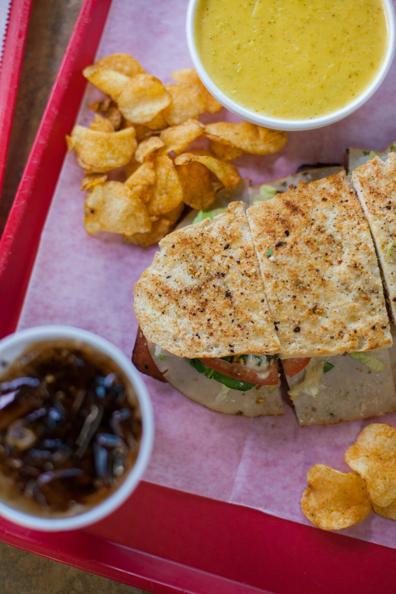 Sandwich with toasted bread, lettuce, and tomato, served with fried chicken pieces and dipping sauces on a pink tray.