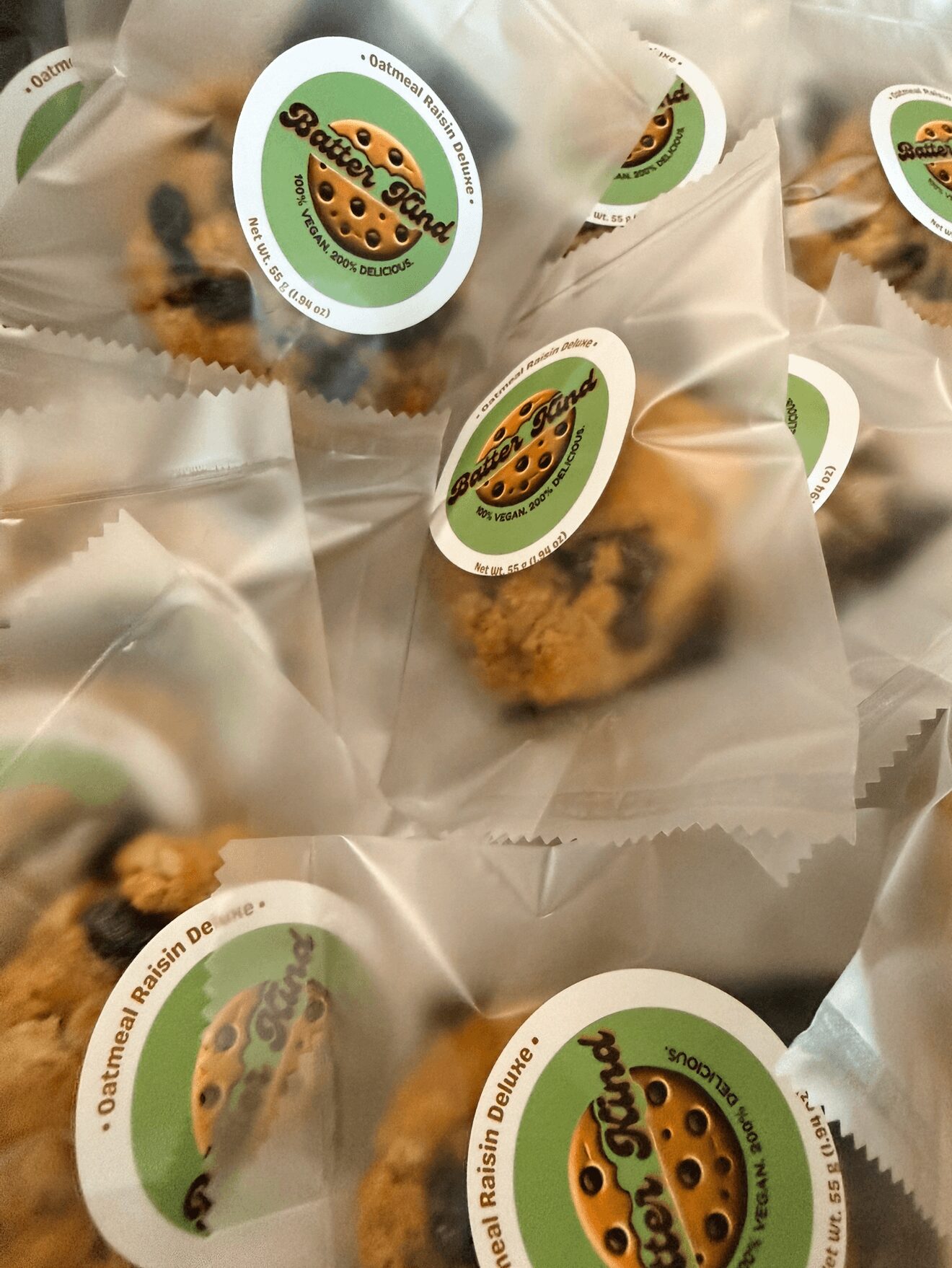 Multiple packaged cookies with a green and white label featuring a cookie illustration, stacked and overlapping.