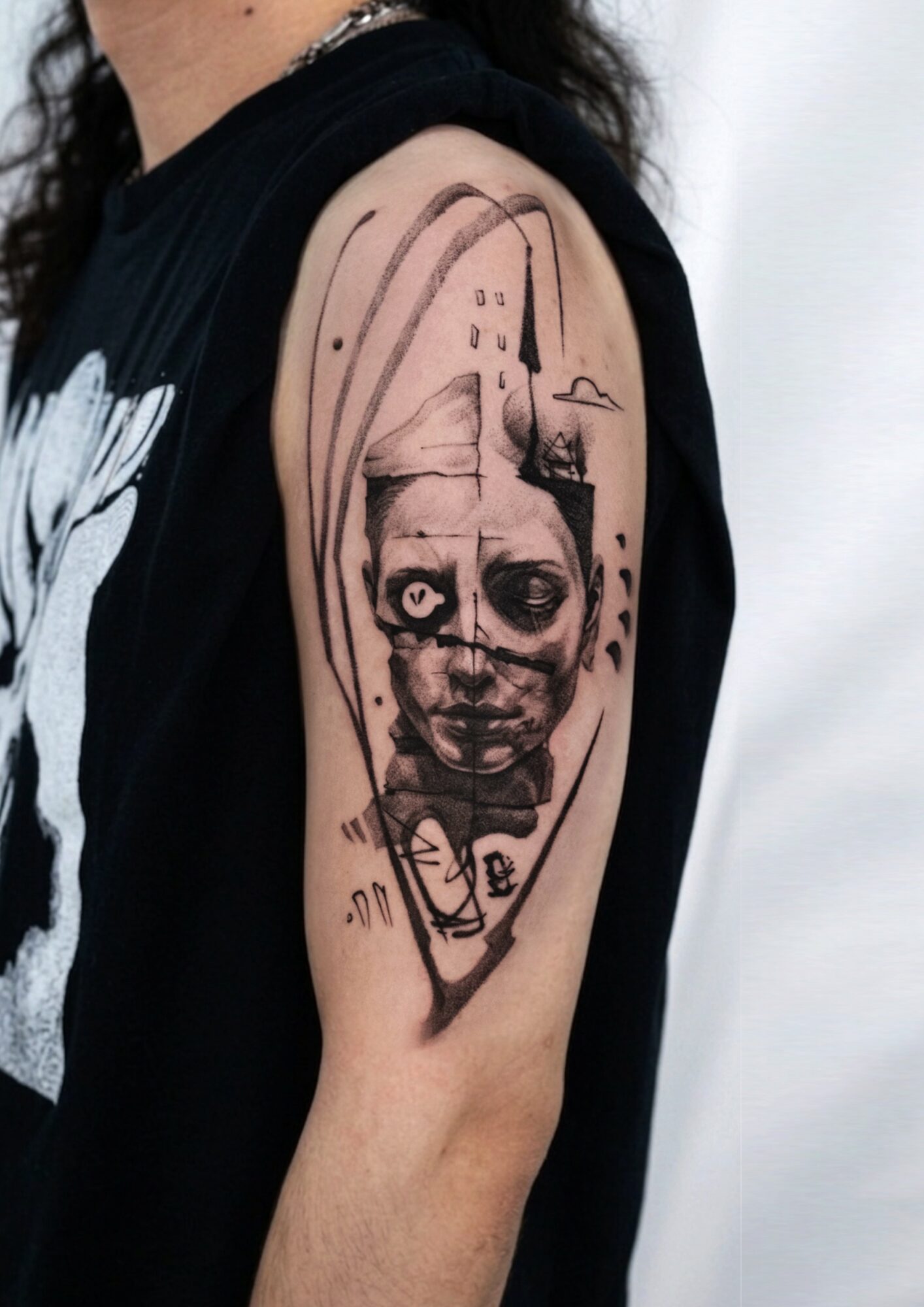 Tattoo of a child's face with large eyes and a serious expression on upper arm, with abstract background elements.