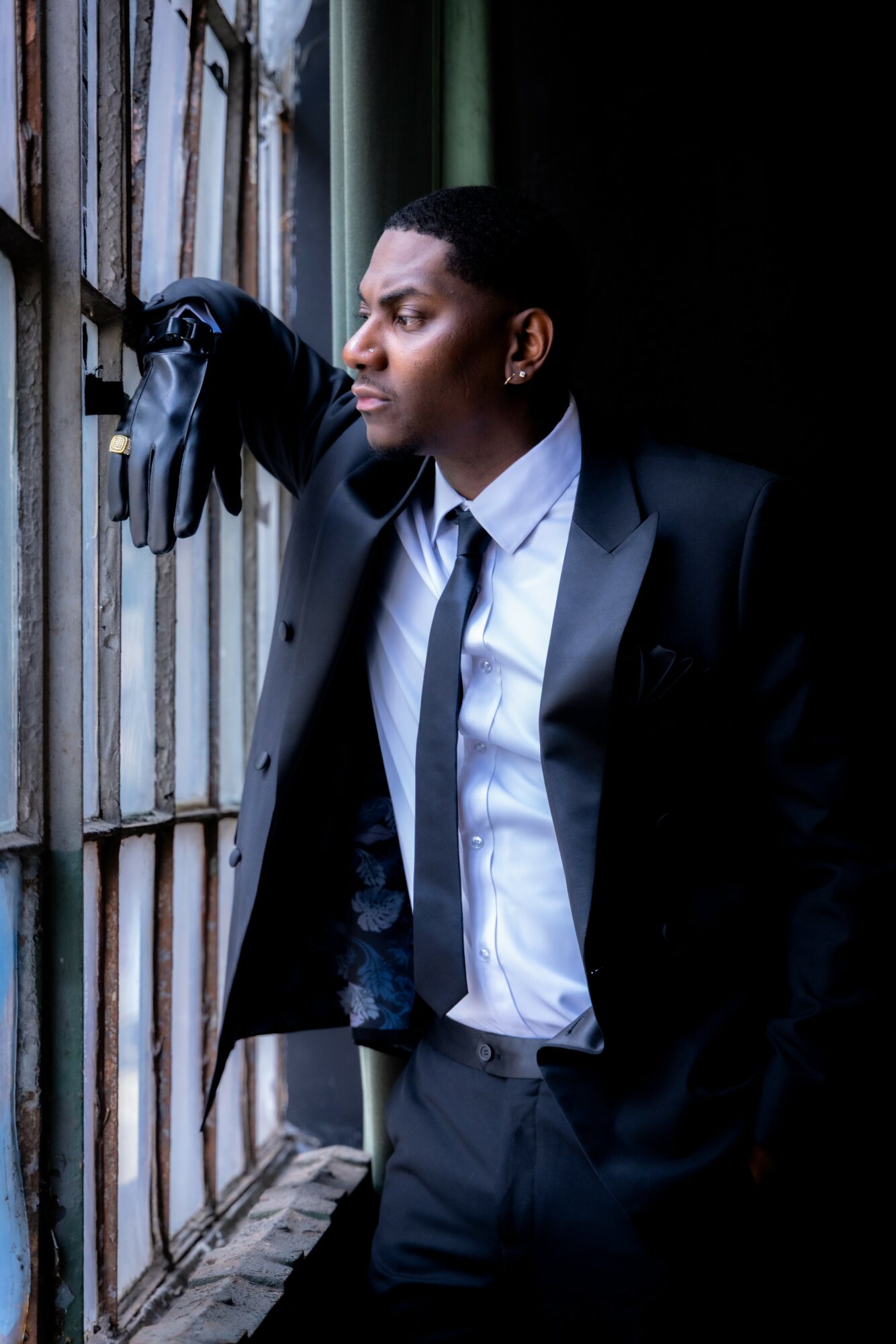 Man in suit and gloves looking out a window with bars, standing indoors near a window with metal bars.