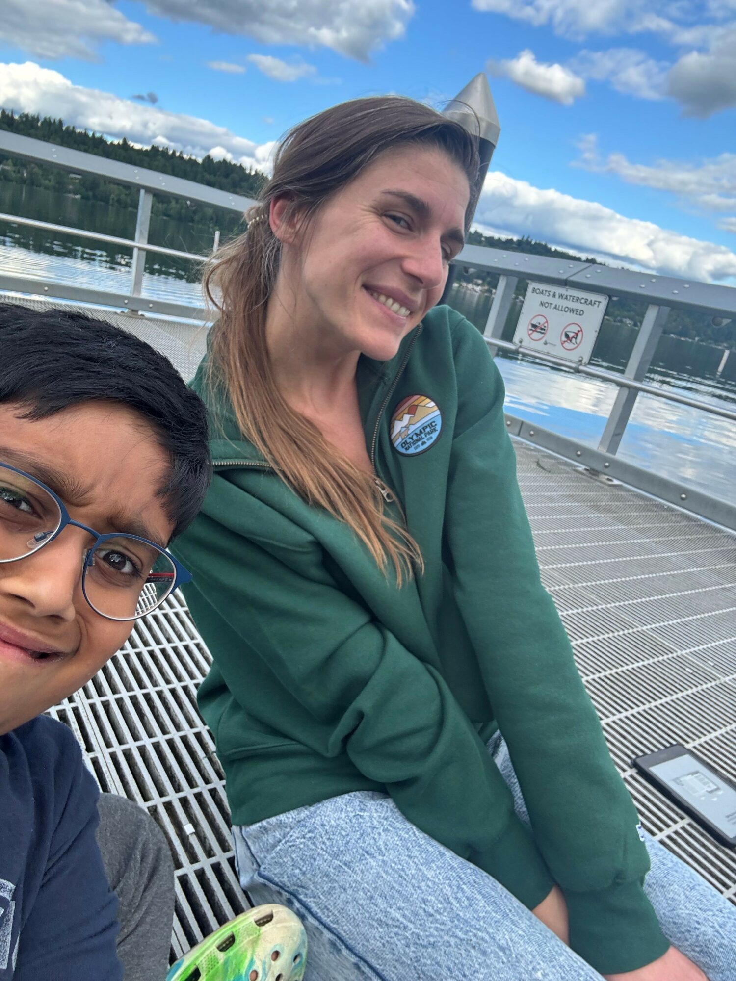 Two women sitting outdoors on a bench, smiling, with a building and sky in the background.