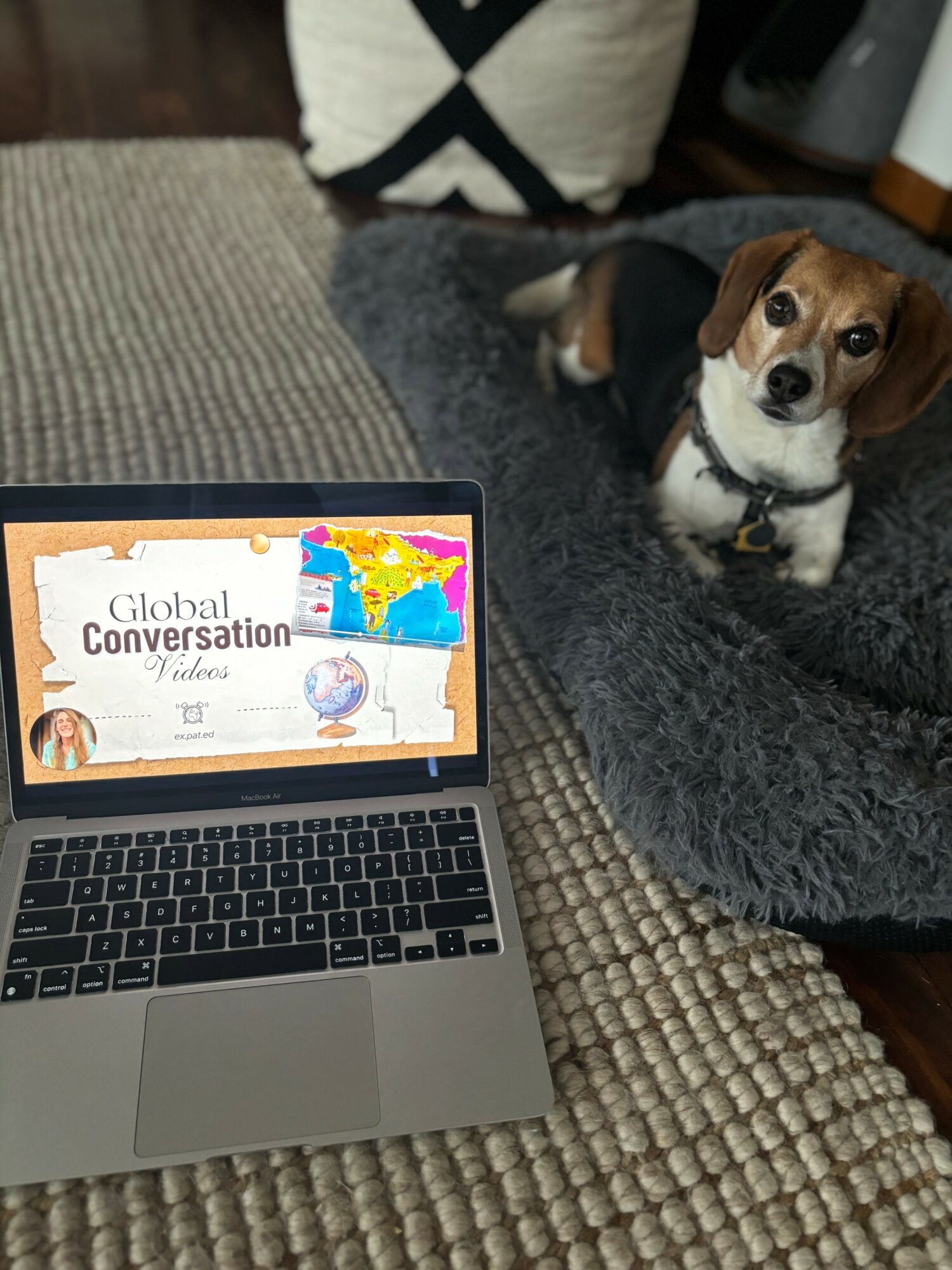 Laptop displaying a presentation titled 'Global conversation' with a dog sitting nearby on a gray blanket.