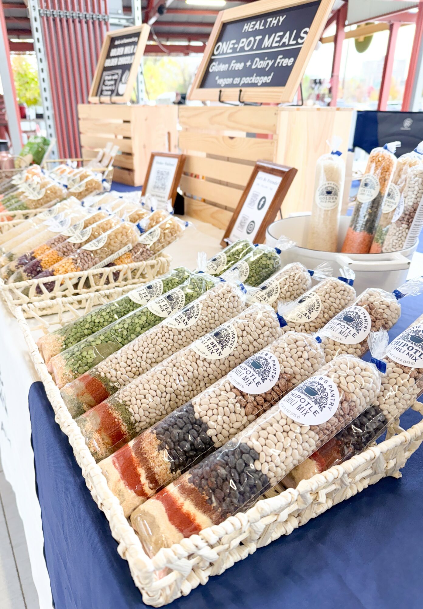 Display of various packaged grains and legumes in a market stall with signs and containers in the background.