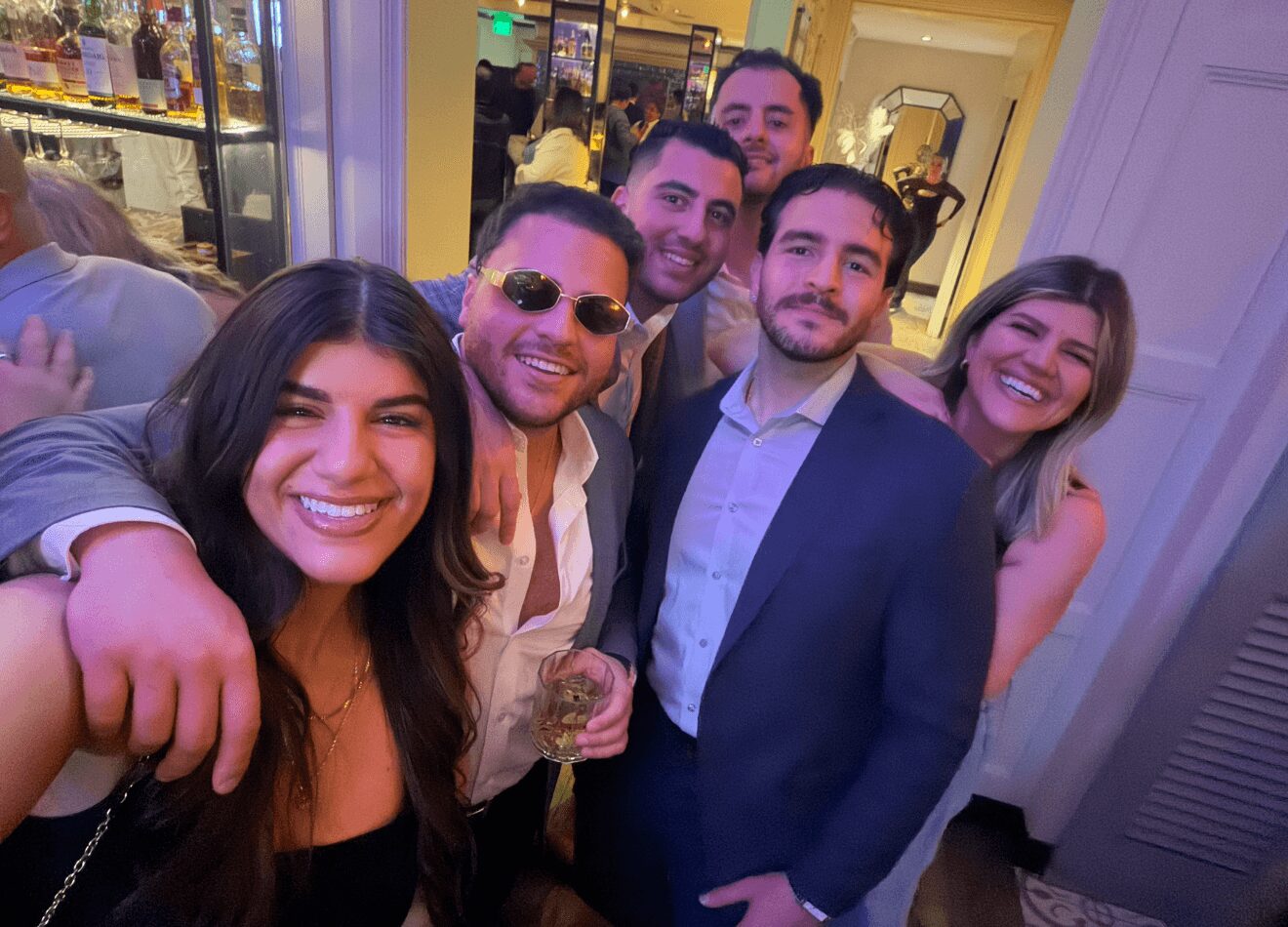 Group of six people smiling and posing together indoors at a social event.