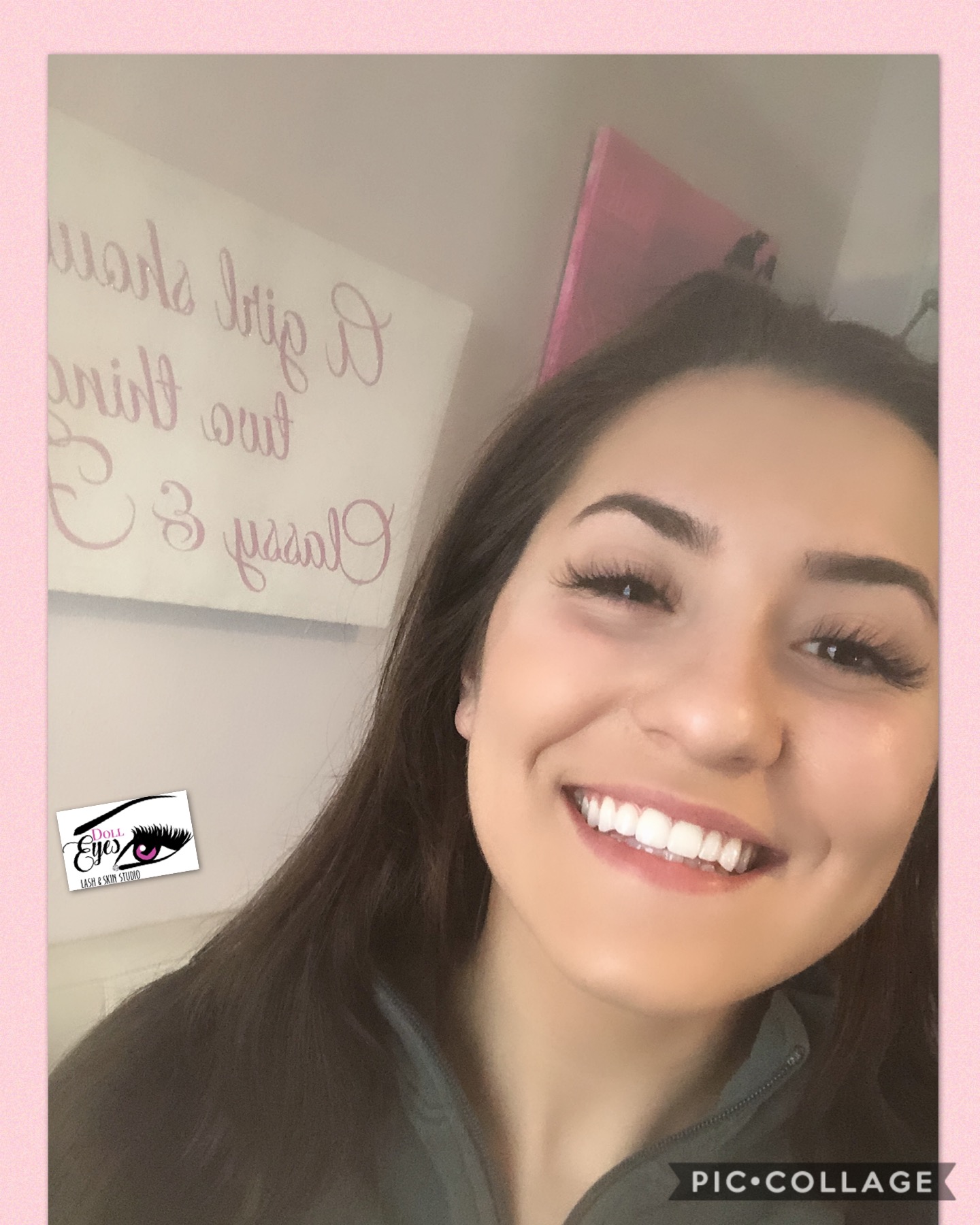Young woman with long dark hair smiling, background includes a whiteboard with pink writing and a pink wall.