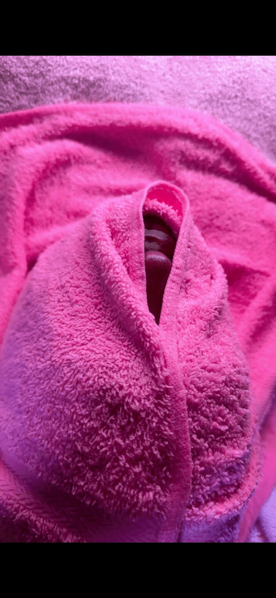Pink towel with a small opening revealing a dark object inside, on a pink surface.