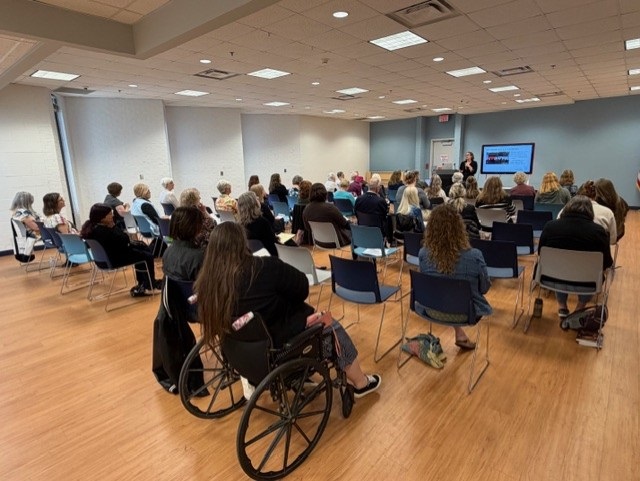 People seated in a conference room watching a presentation on a screen at the front.