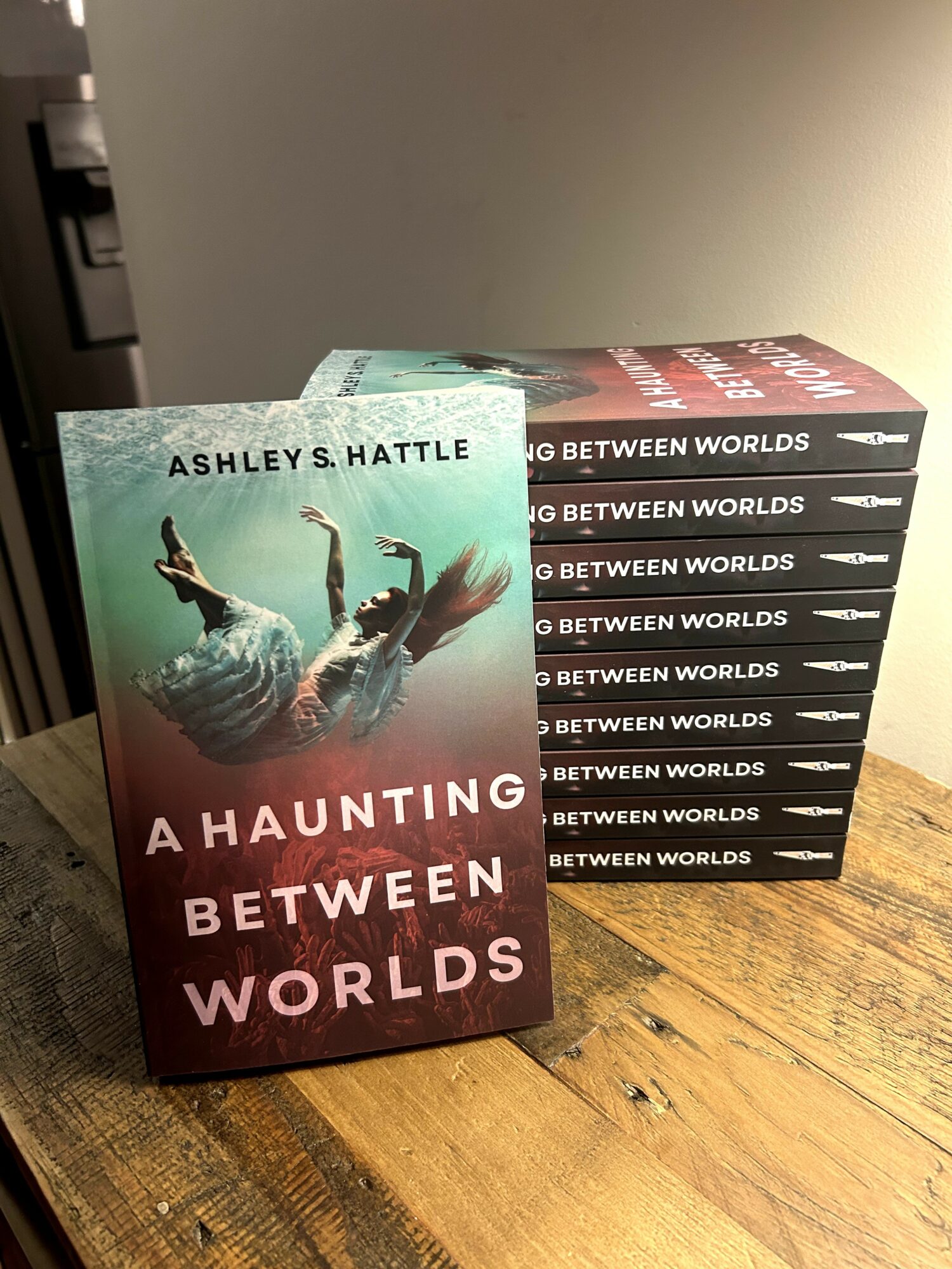 Book titled 'A Haunting Between Worlds' with a person floating upside down on the cover, placed on a wooden surface.