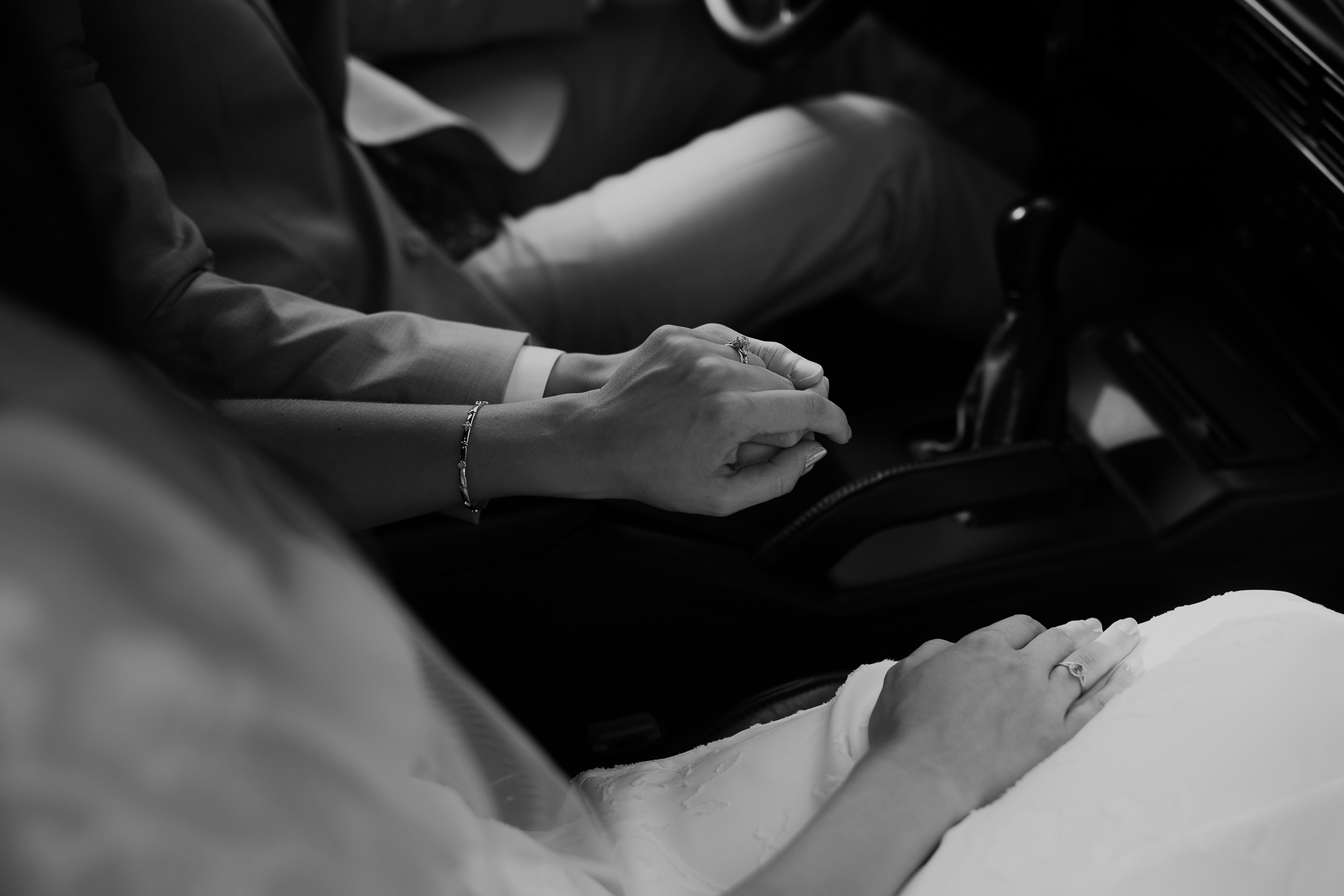 Two people sitting in a car, holding hands on the center console, in black and white.