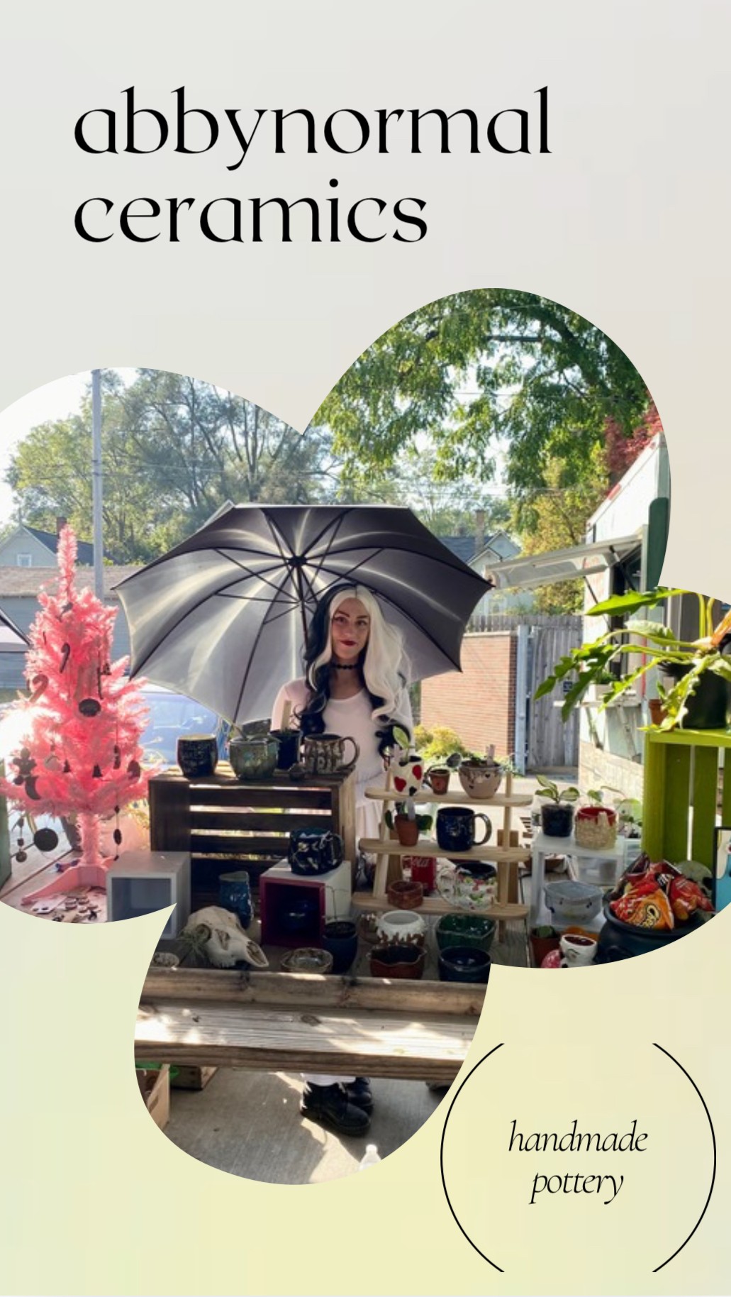 Person sitting at a table with ceramics, holding an umbrella outdoors, decorated with plants and Christmas tree, sunlight streaming in.