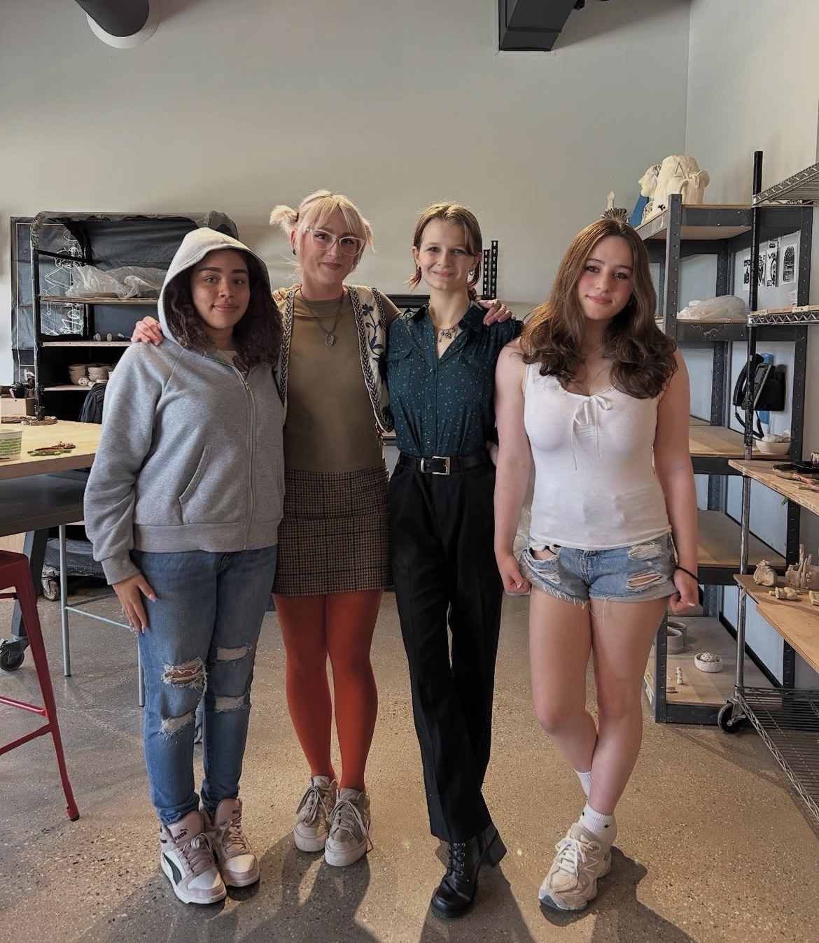 Four women standing together in a room with shelves and equipment, smiling at the camera.