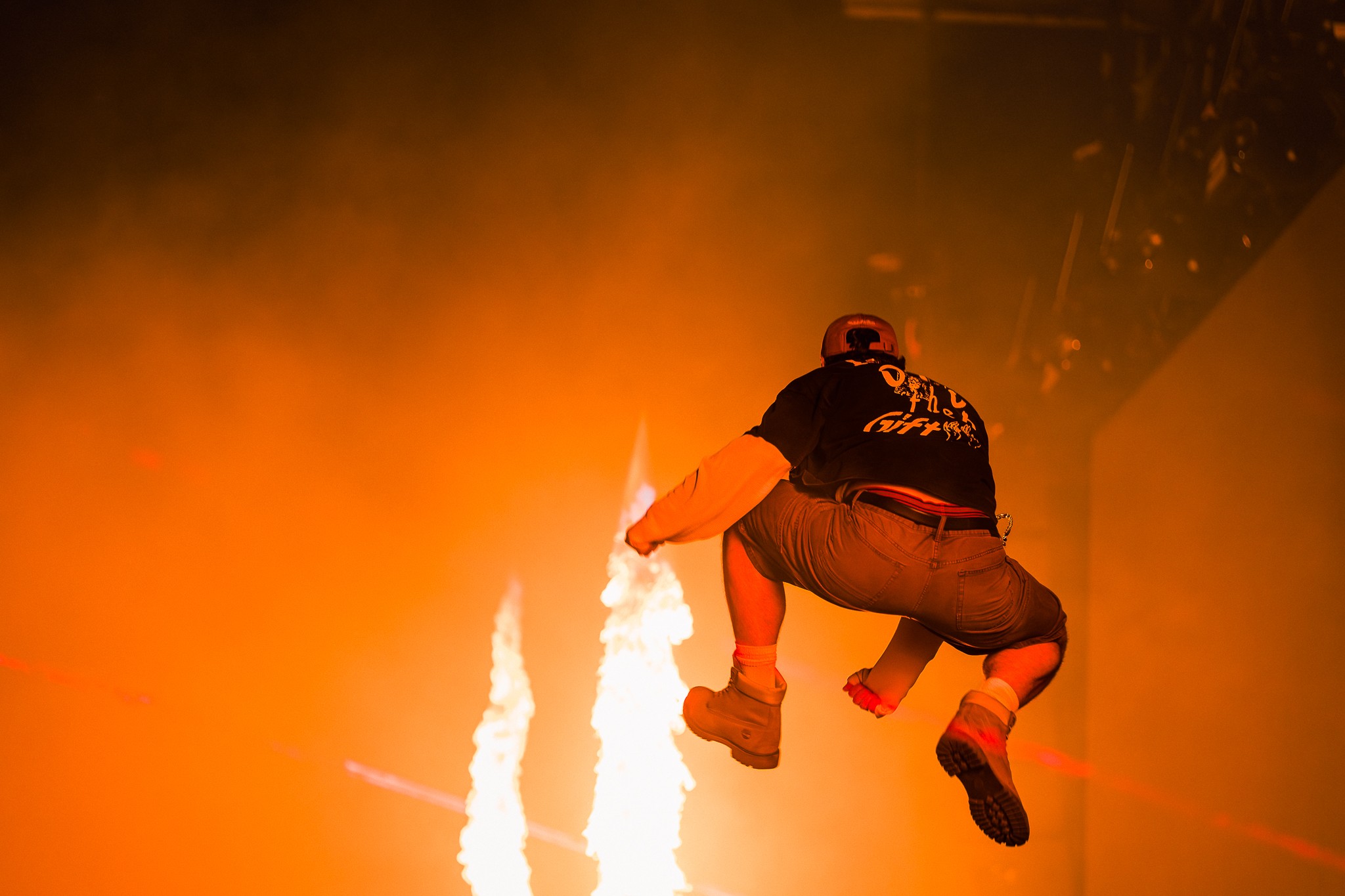 Person jumping in front of a fiery background with flames and sparks flying, wearing a helmet and protective gear.