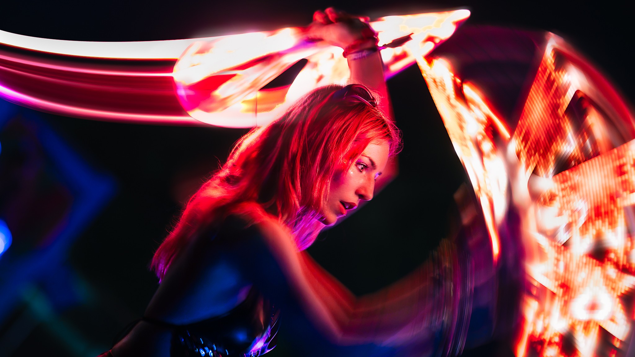 Person with long hair performing with colorful light trails in a dark setting.