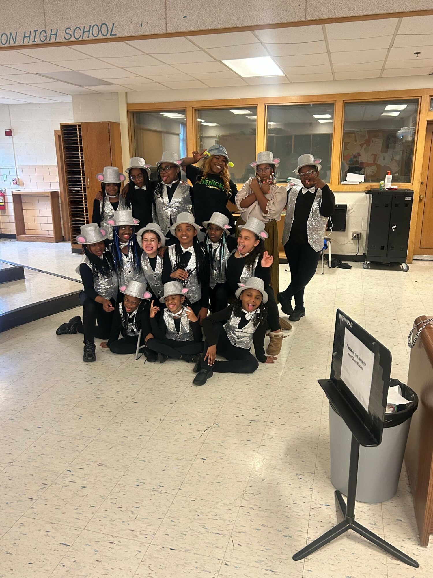 Group of people in formal attire posing indoors, some wearing masks, with a music stand nearby.
