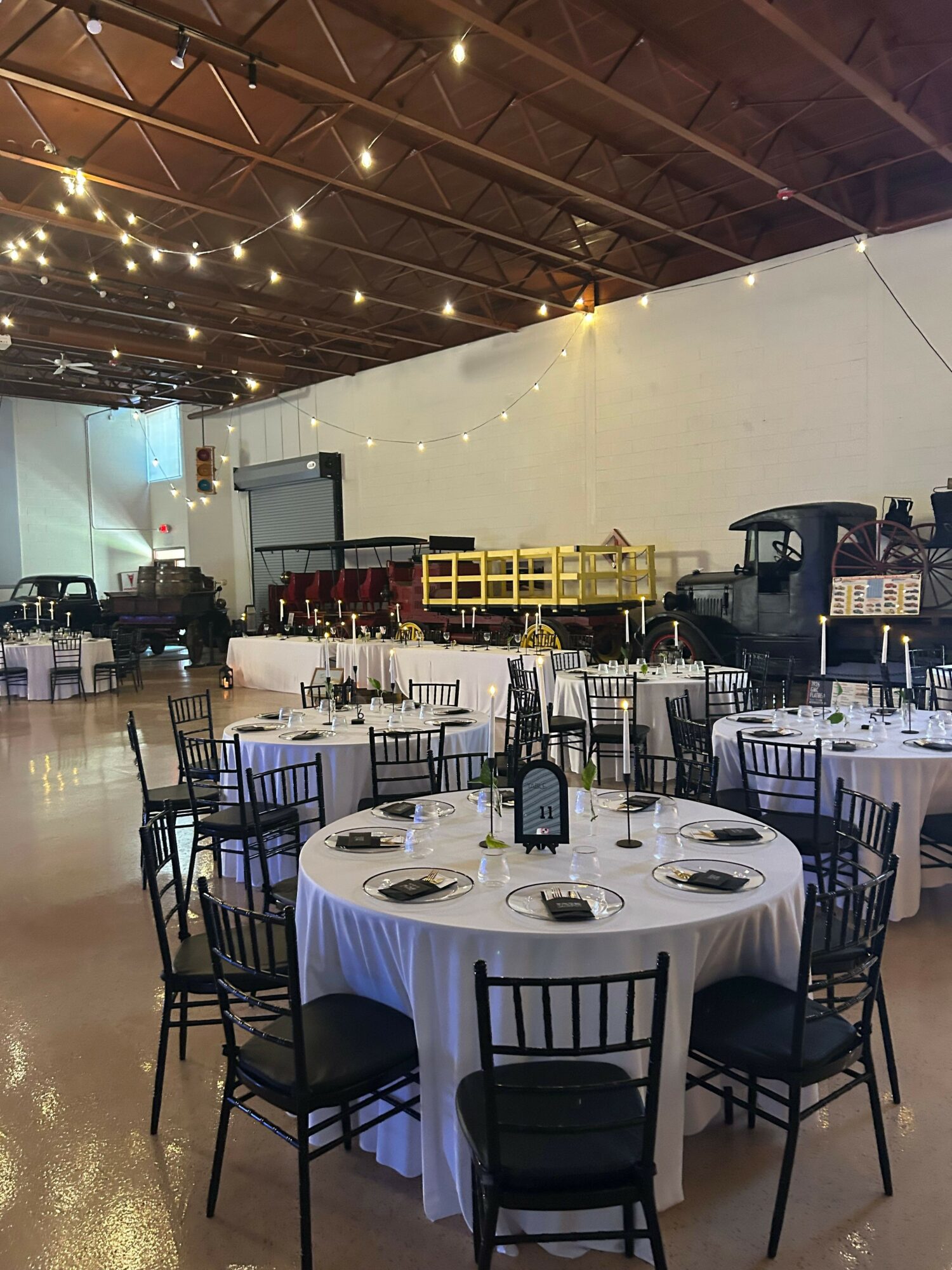 Round table set with plates, glasses, and utensils in a banquet hall with chairs and decorations.