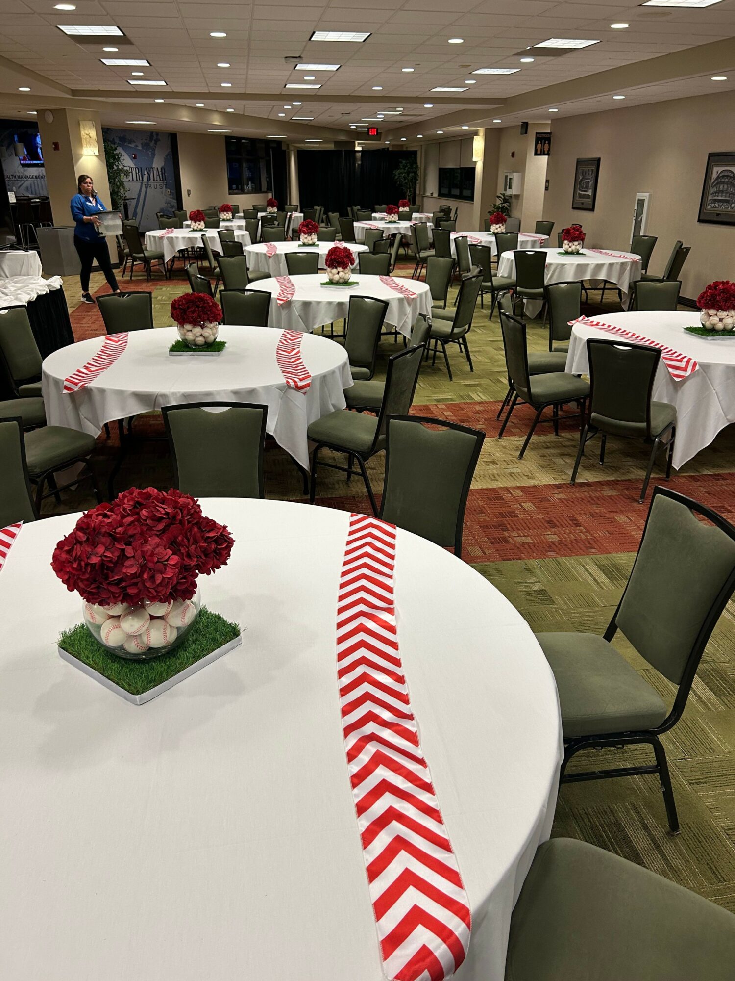 Round table with a red and white chevron table runner, floral centerpiece, and place settings, in a decorated banquet hall.