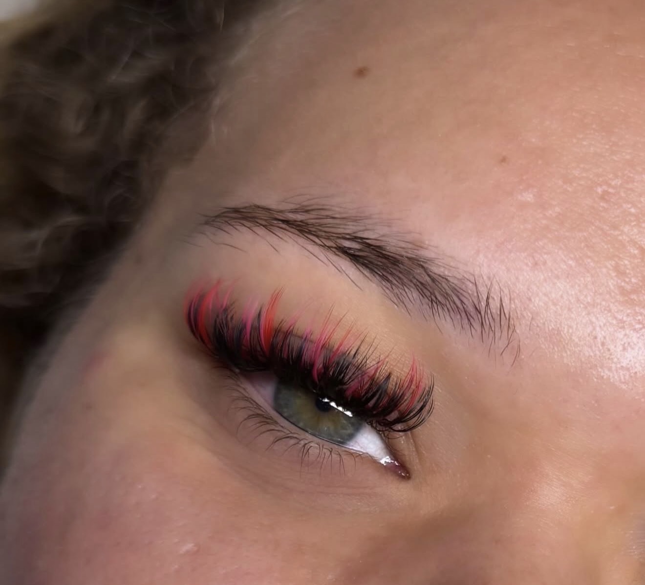 Close-up of a person's eye with colorful, long eyelashes and well-groomed eyebrow.