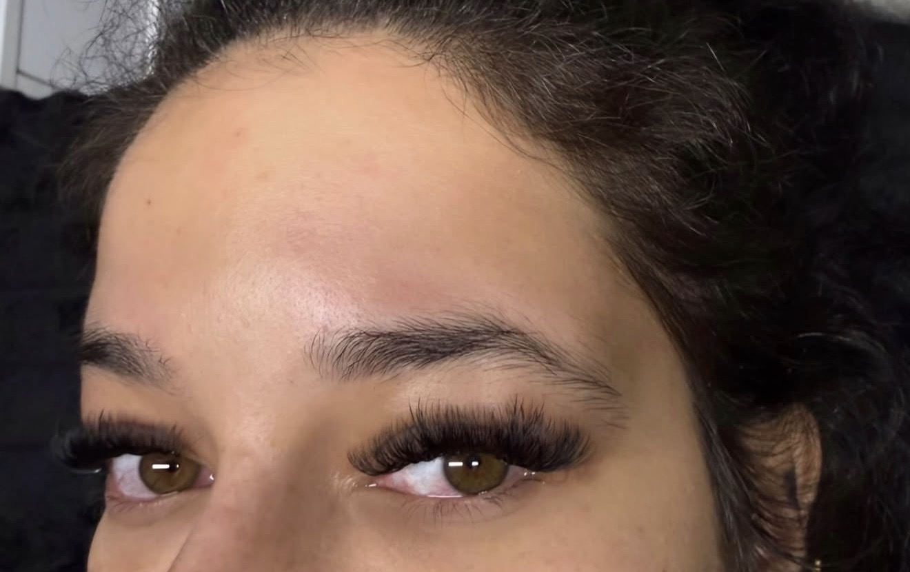 Close-up of a person's forehead, eyes, and eyebrows with makeup and long eyelashes.