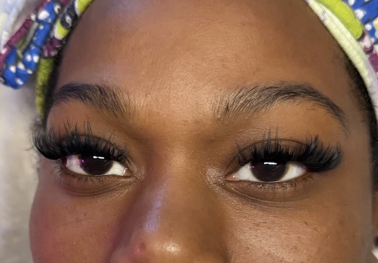 Close-up of a person's eyes with long eyelashes and colorful headscarf, showing smooth skin and well-groomed eyebrows.
