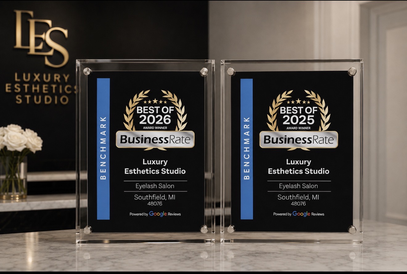 Two glass awards with 'Best of 2025' and 'Business Rate' logos, placed on a table in front of a sign for a luxury esthetic studio.