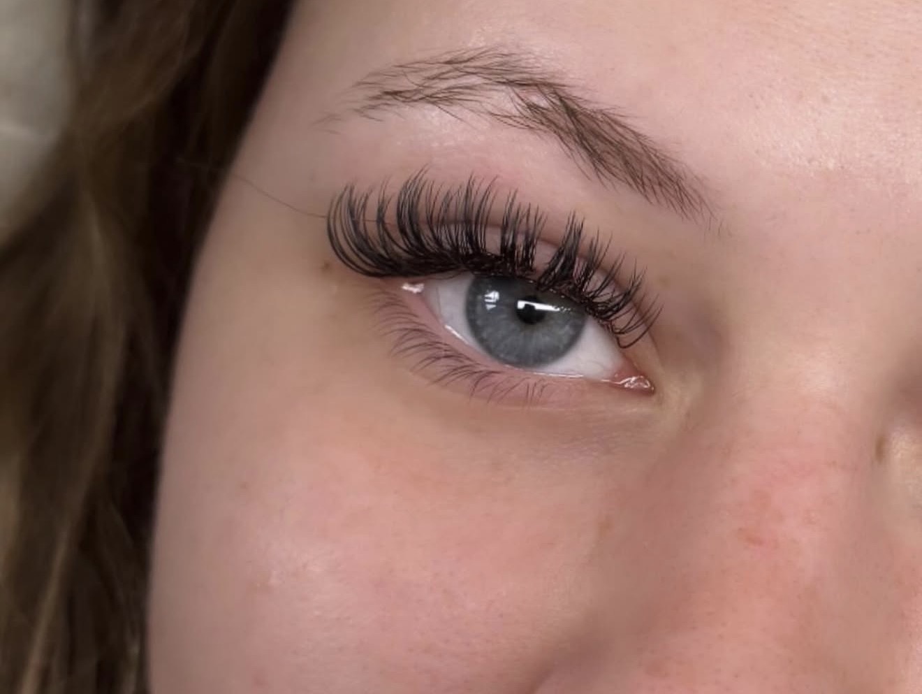Close-up of a person's eye with long, curled eyelashes and light blue iris.