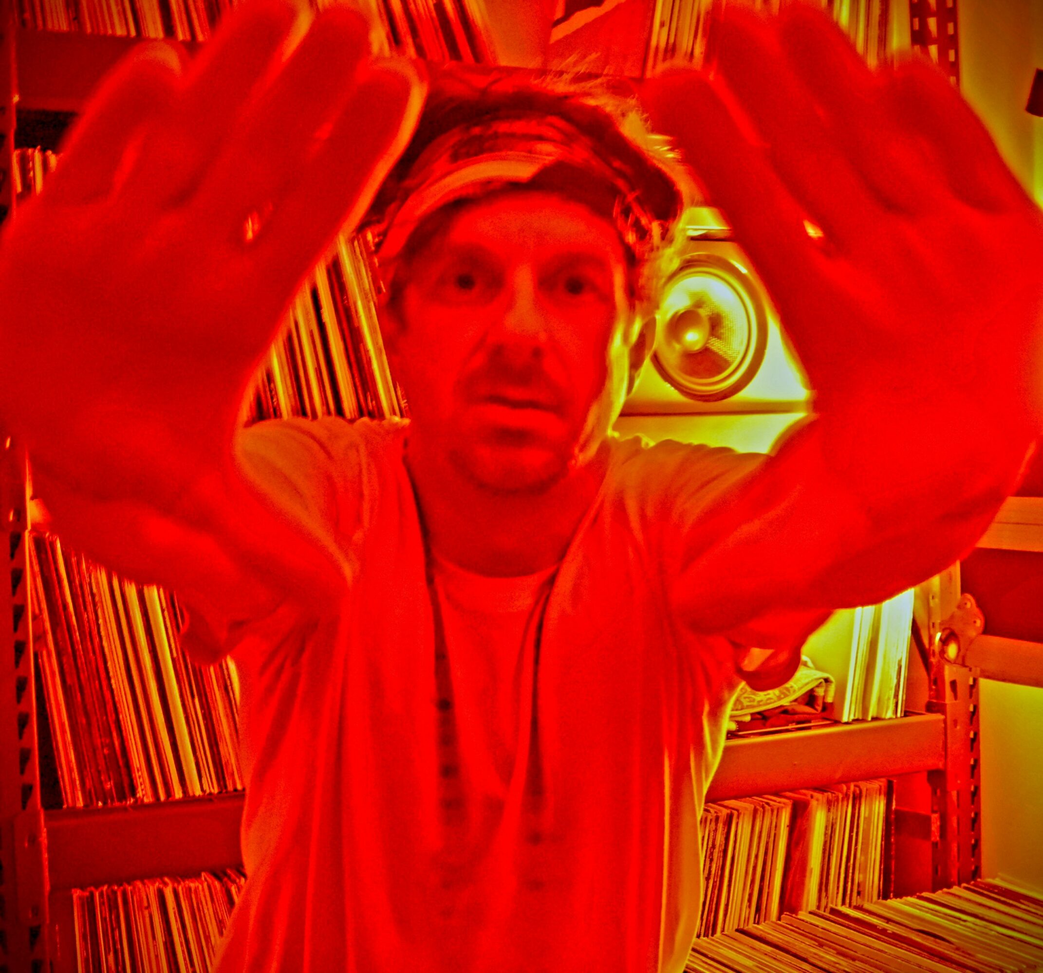Person with hands close to camera, looking at the viewer, surrounded by bookshelves, in a room with warm lighting.